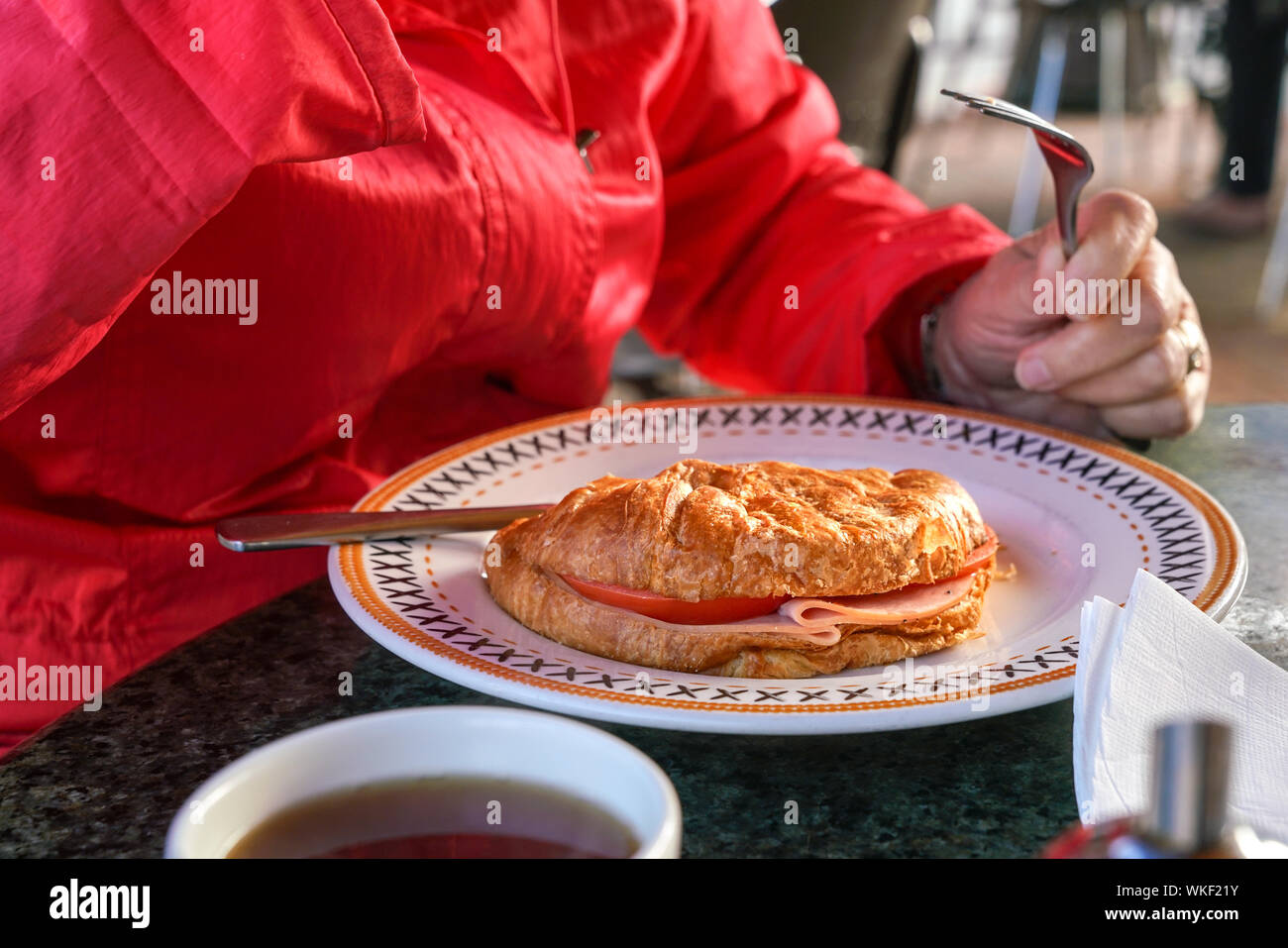 Donna di mani con cucchiaio e forchetta per mangiare croissant con uova e pancetta Foto Stock