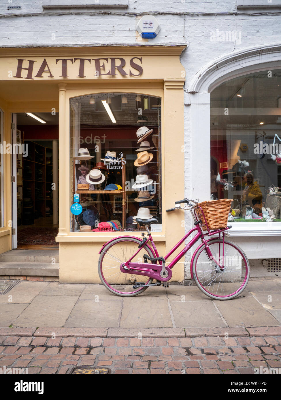 Una bicicletta rosa con un cestello appoggiato contro un muro esterno Lairds Hatters hat shop in Green Street Cambridge Regno Unito Foto Stock
