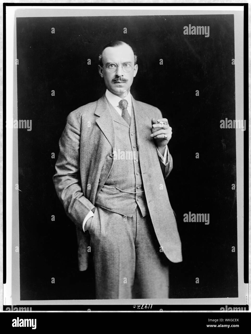 John Barry Ryan, tre quarti di lunghezza verticale, in piedi, rivolto verso la parte anteriore, tenendo sigaretta Foto Stock