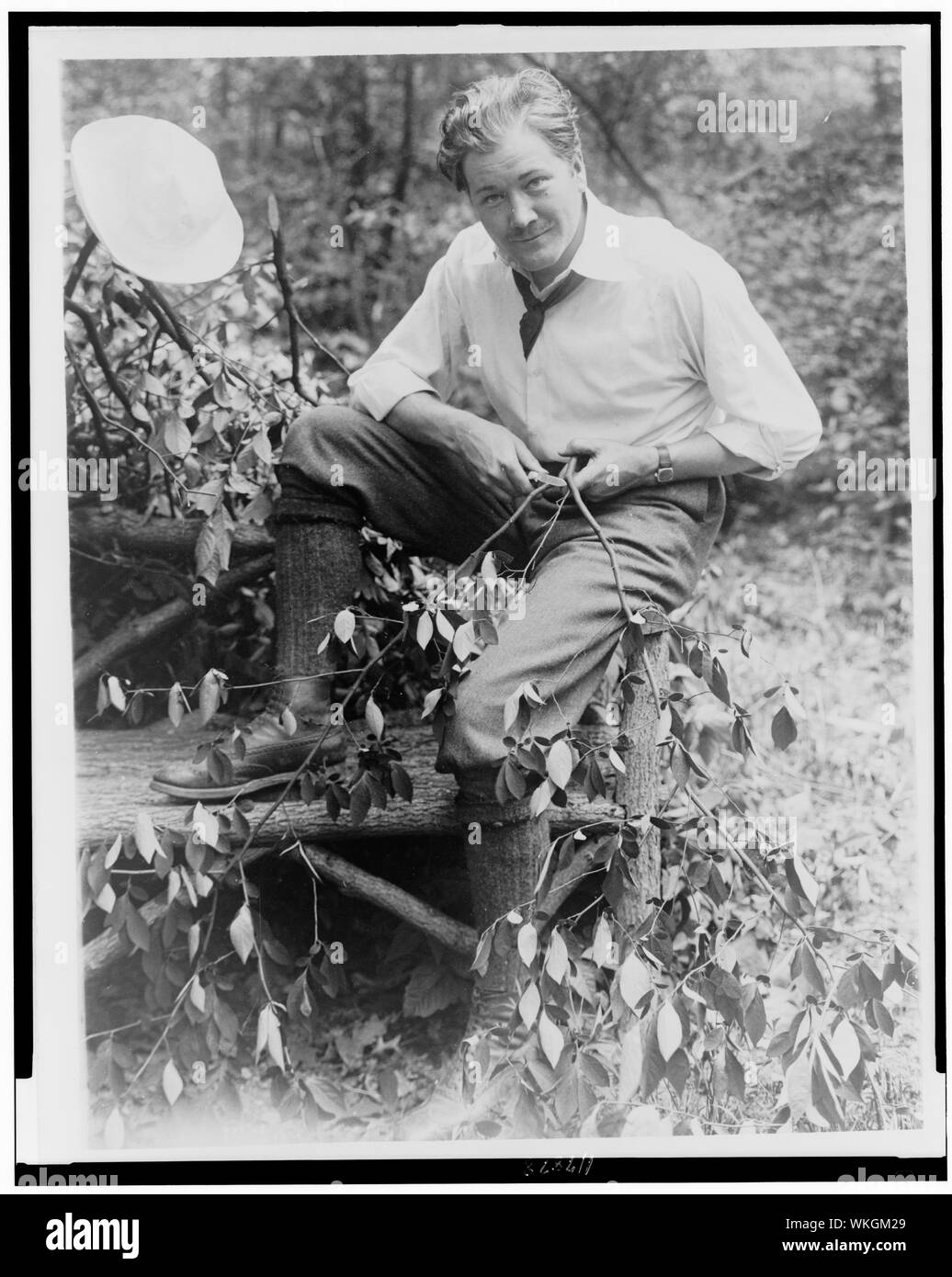 John Charles Thomas, cantante, ritratto a figura intera, seduti su una panchina del registro, whittling una filiale di piccole dimensioni Foto Stock