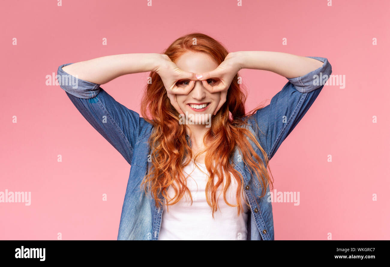 Giocoso redhead girl tenendo le dita vicino agli occhi come gli occhiali Foto Stock