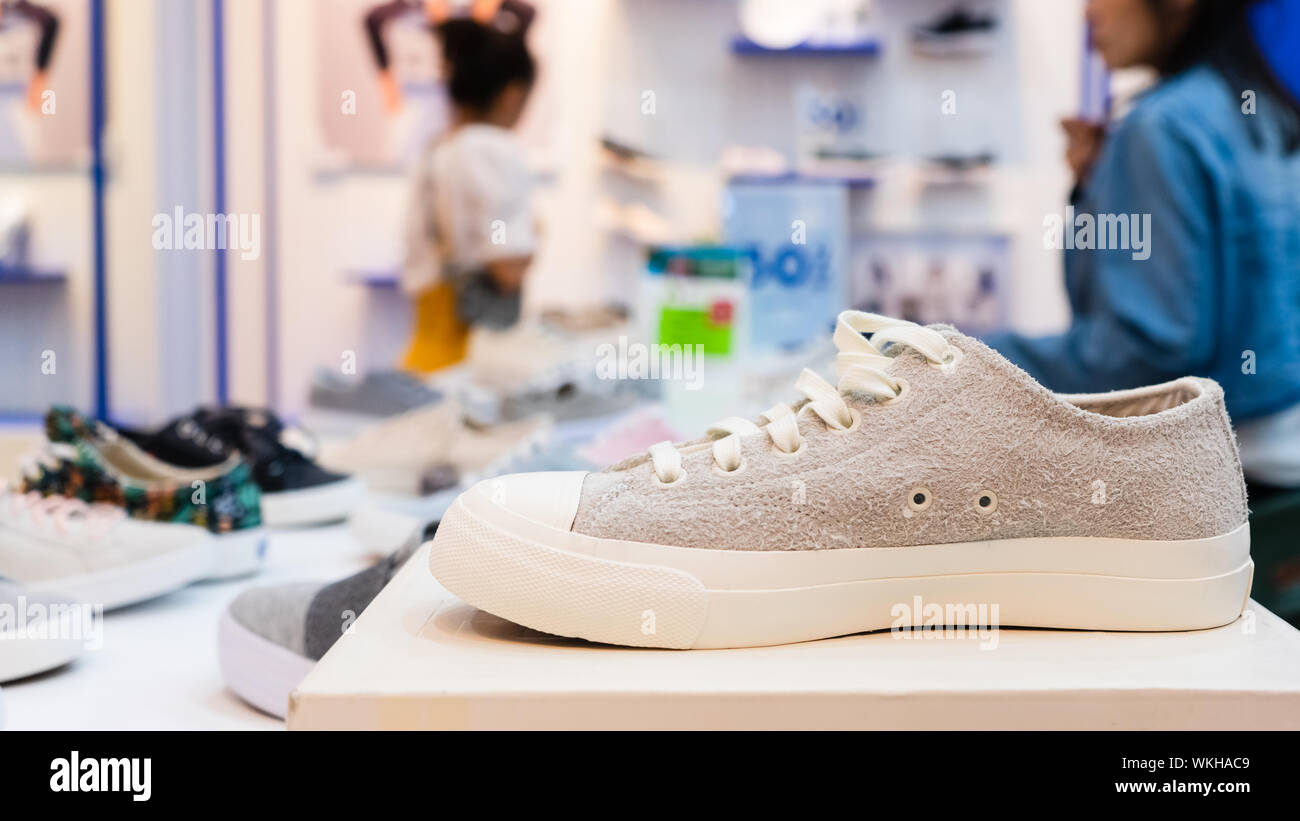 Sneakers bianco sulla tabella di visualizzazione nelle scarpe fashion store, close-up con sfondo sfocato dell'acquirente. I nostri clienti nel negozio di calzature con moderni stylis Foto Stock