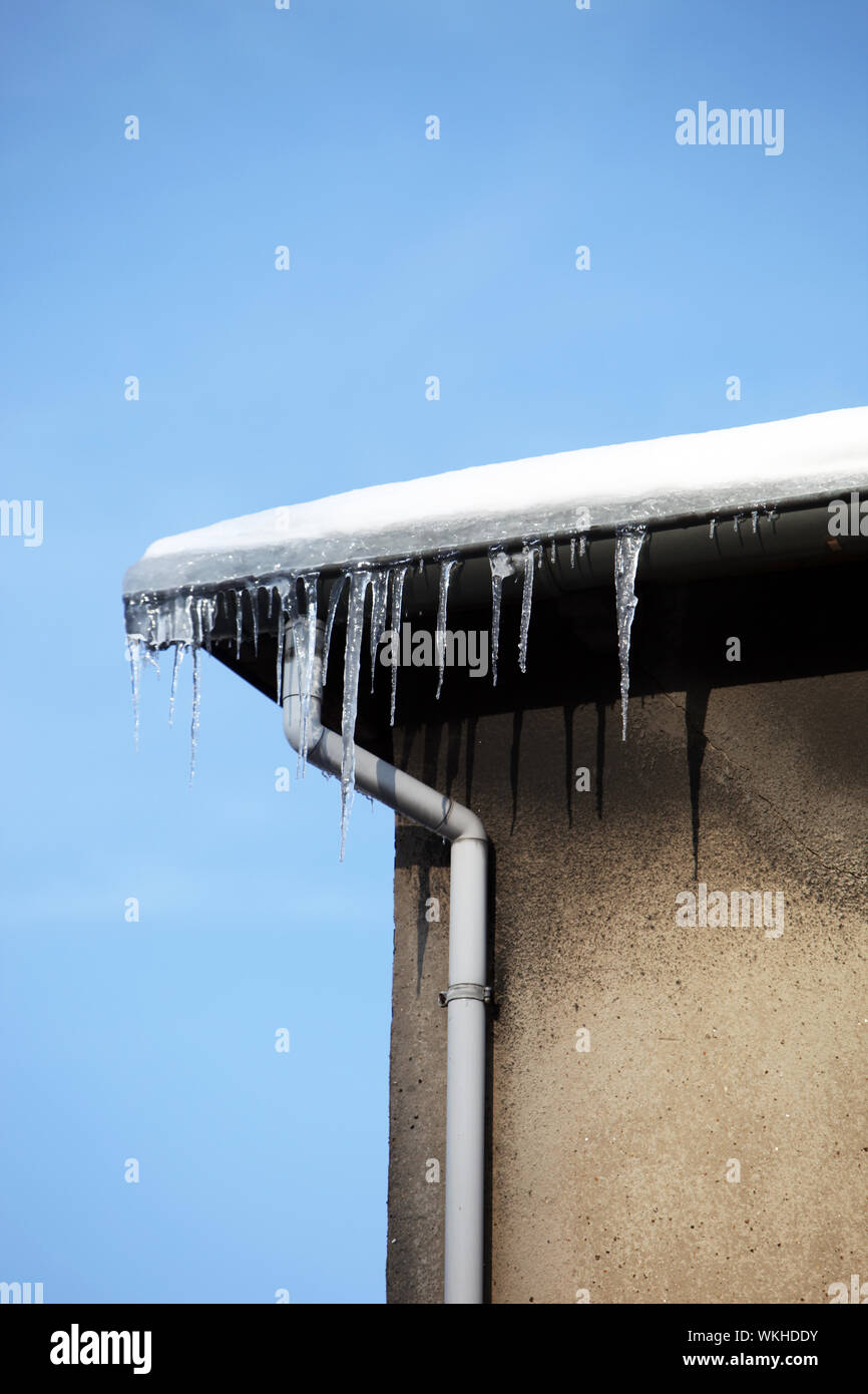 Piccoli ghiaccioli appesi al cornicione di una casa contro un cielo blu con spazio per il testo Foto Stock