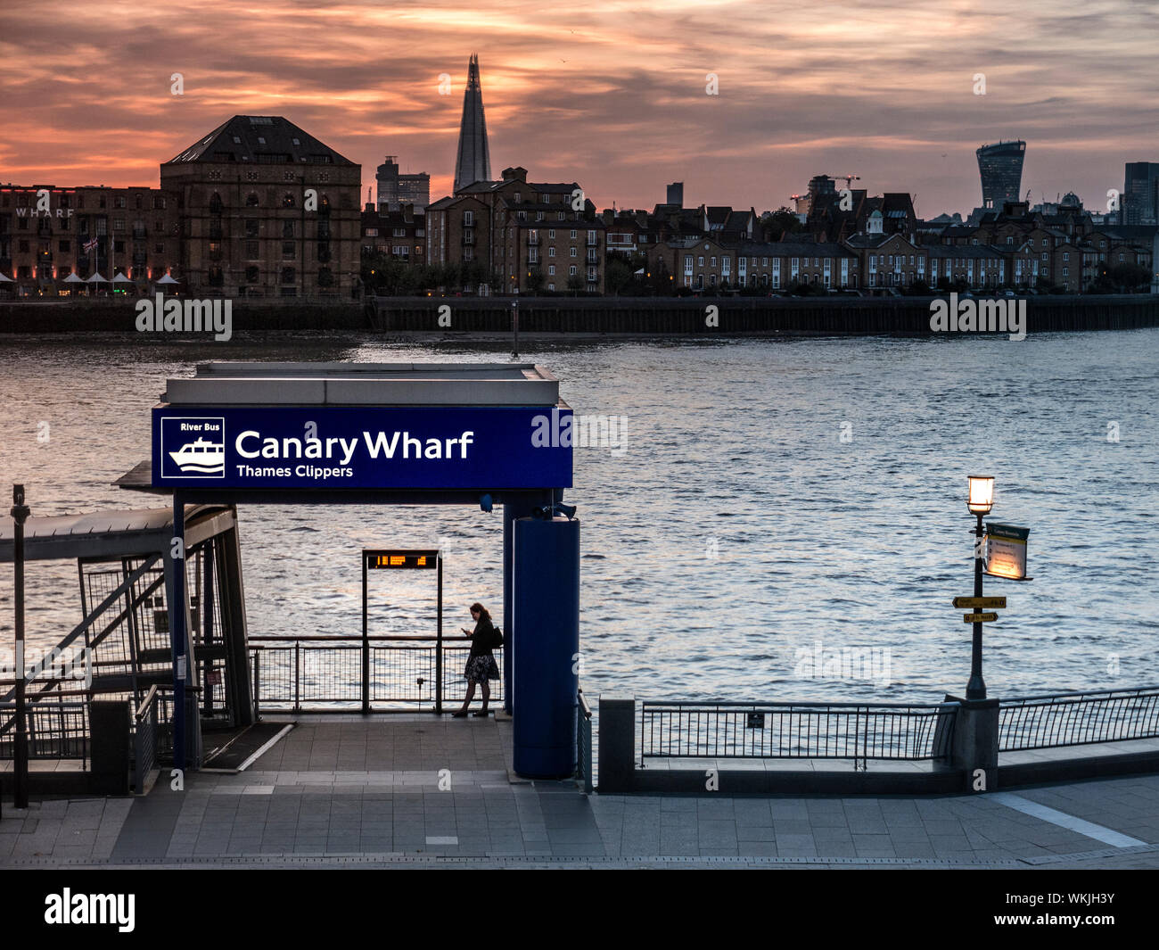 Canary Wharf femmina città silhouette lavoratore utilizzando solo il dispositivo smartphone in barca sul fiume punto di imbarco molo al tramonto London Shard e "walkie talkie' edificio in background London E14 Foto Stock