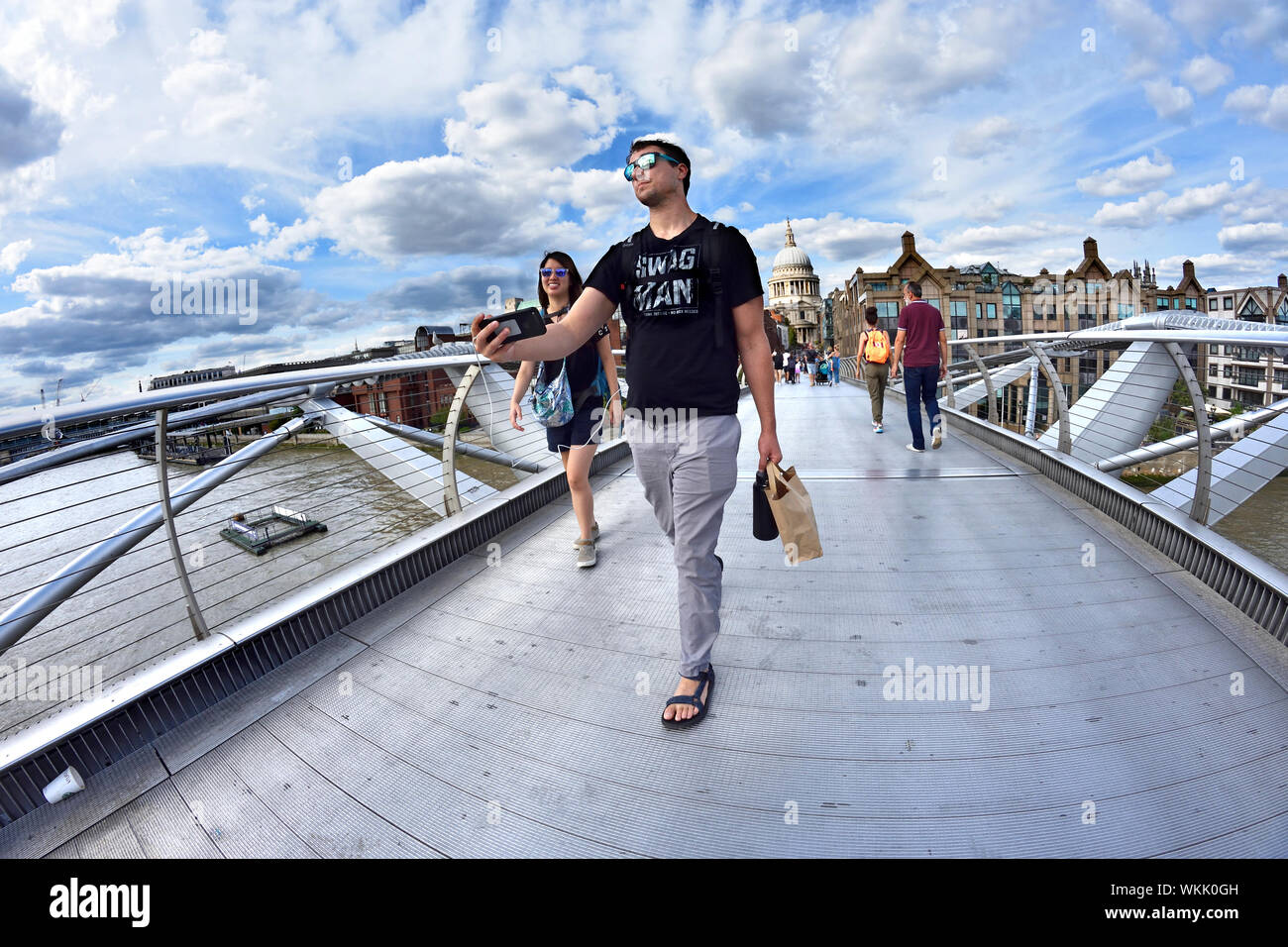 Londra, Inghilterra, Regno Unito. Le persone che attraversano il Millennium Bridge in una giornata di sole in agosto - uomo prendendo un selfie o un video Foto Stock