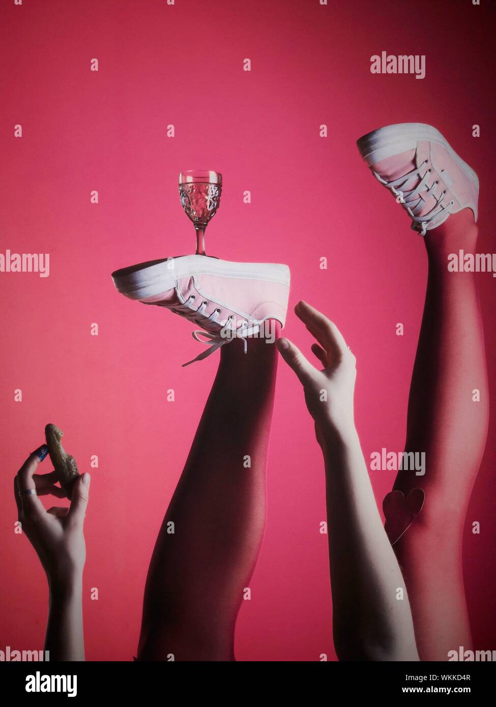Sezione bassa della donna che indossa le scarpe mentre il vetro di bilanciamento sul piede contro sfondo rosa Foto Stock
