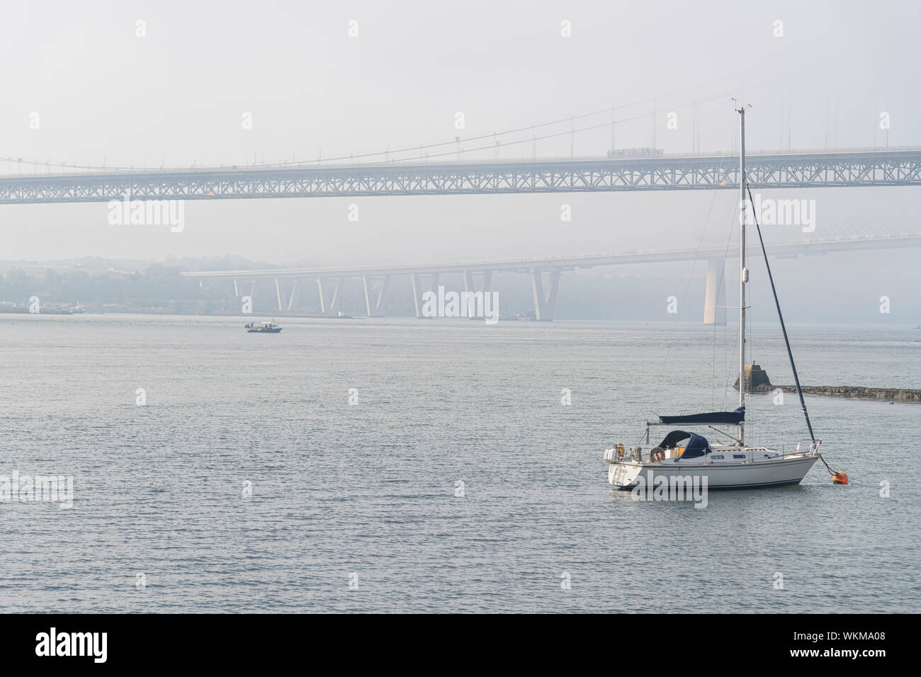 Una piccola barca a vela con entrambi Forth Road Bridge in background Foto Stock