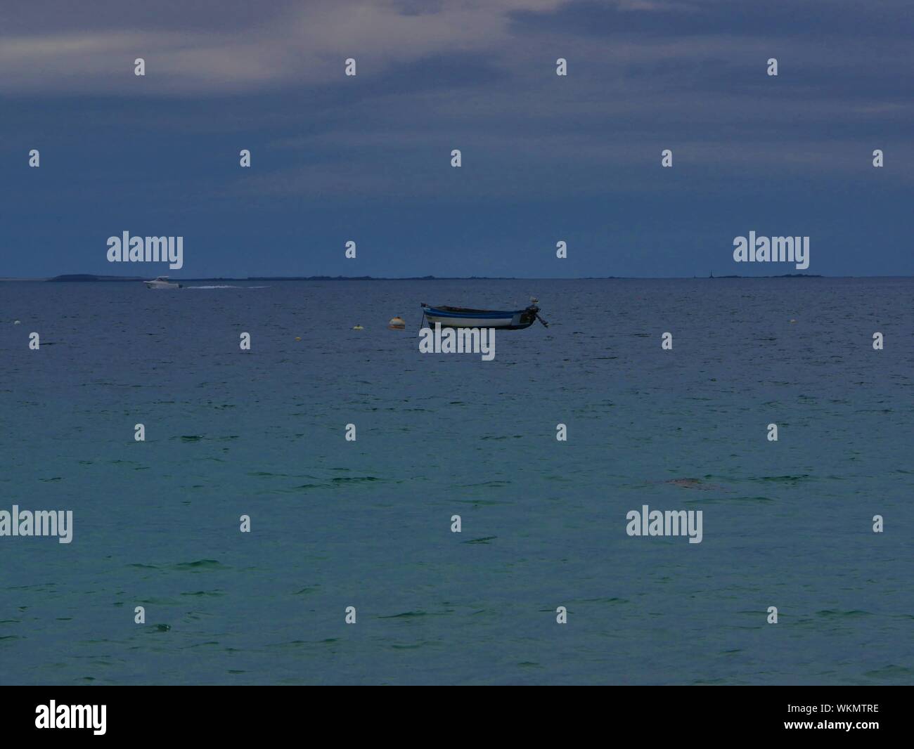 Barca bleue et blanche , ancrée devant la plage de plouguerneau , en arrière plan une île deserte , eau bleue turchese Foto Stock