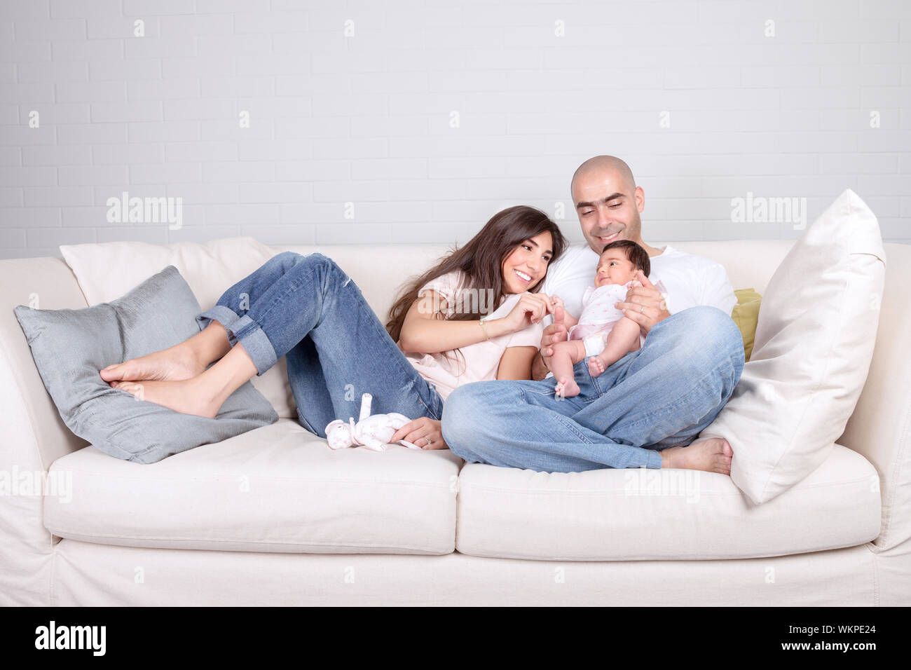 I giovani genitori con piccolo bambino a casa seduti sul divano accogliente, godendo di famiglia, amare giovane con la figlia del neonato, positività e concetto di divertimento Foto Stock