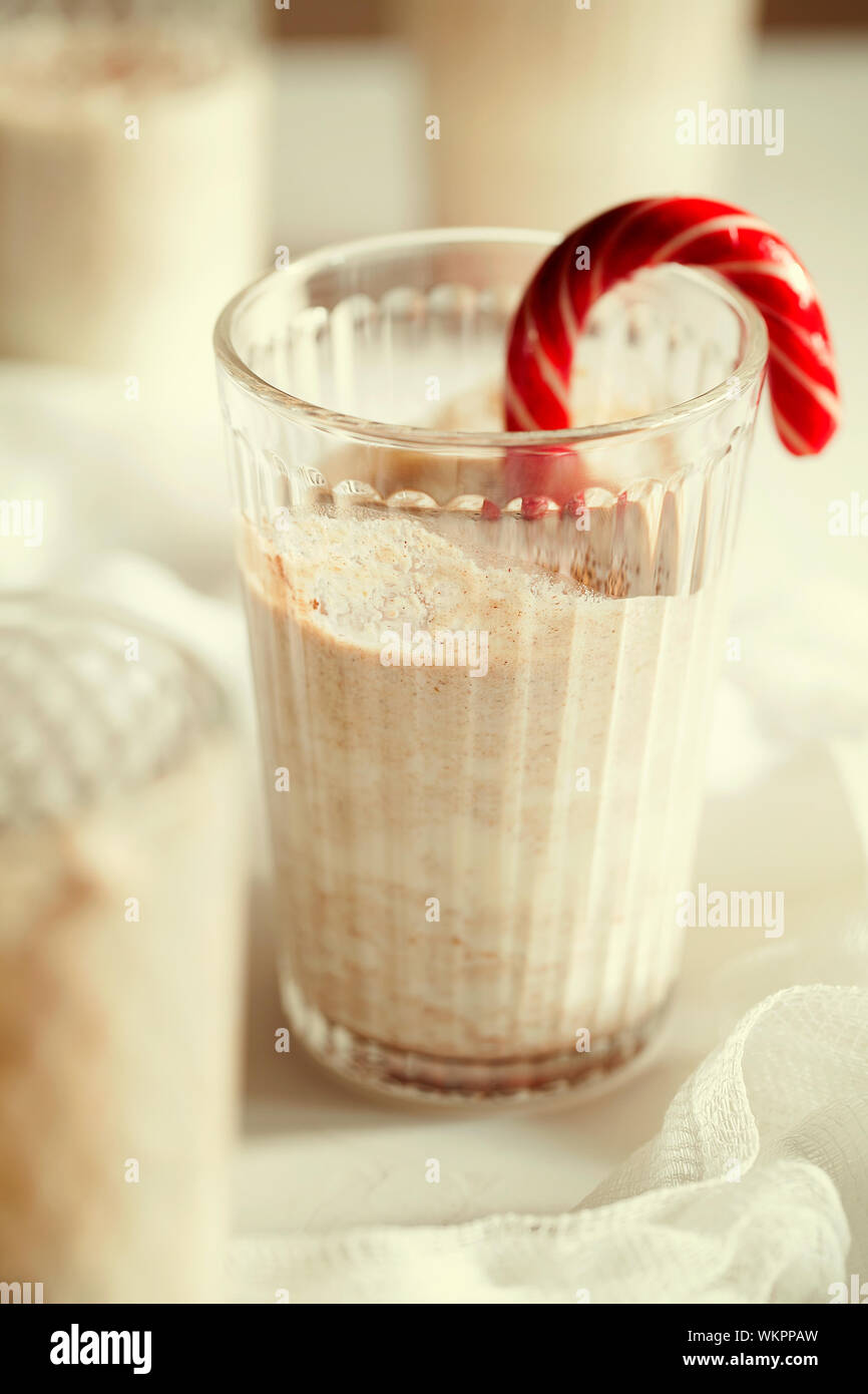 Tradizionale winter in casa gustosi cocktail di Natale zabaione con latte, il rum e la cannella e la noce moscata decorate candy cane su sfondo bianco Foto Stock