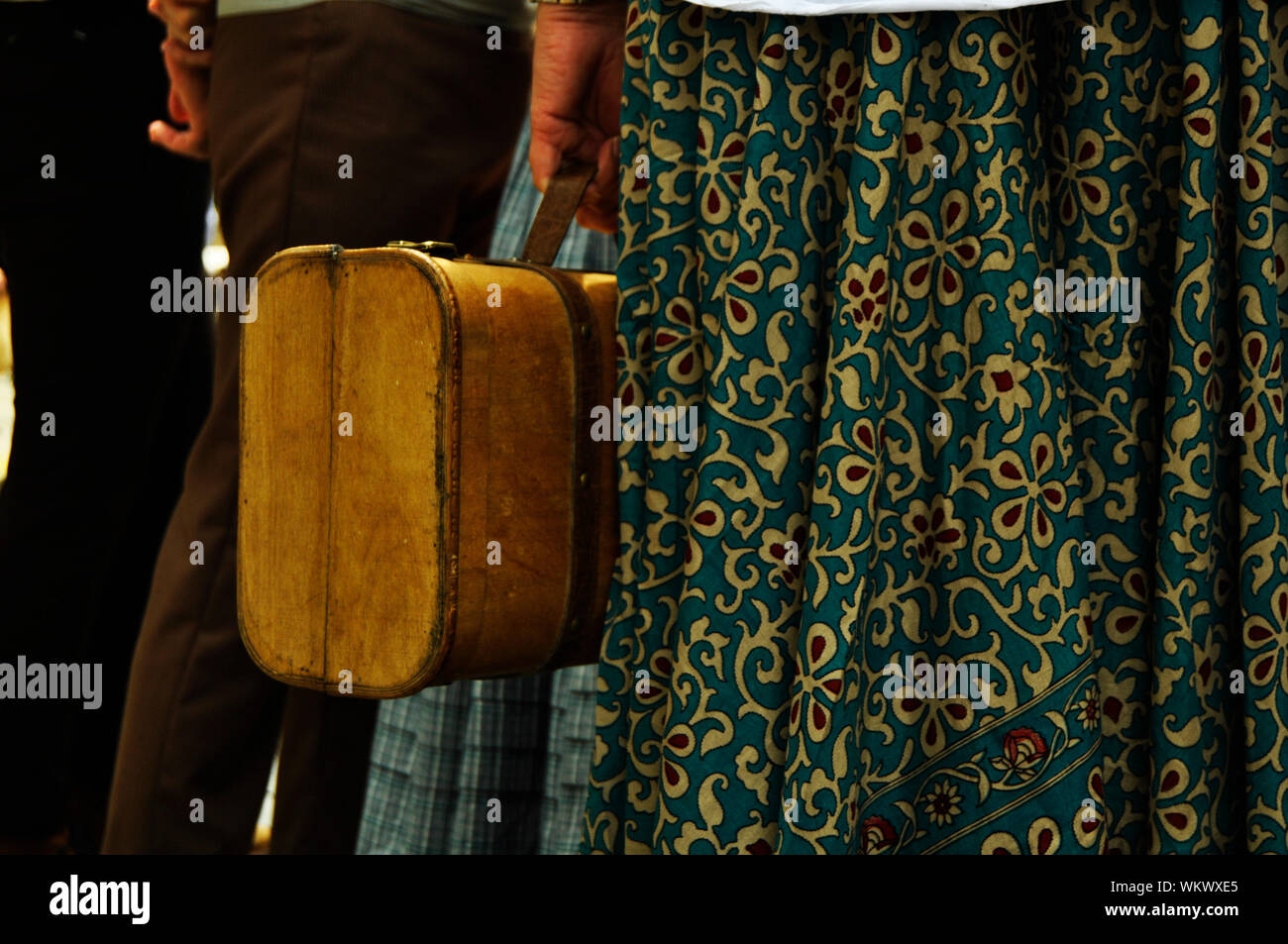 Donna in possesso di una valigia vintage / Donne che indossano una gonna grande con fiori e che tengono un vecchio bagaglio a mano Foto Stock