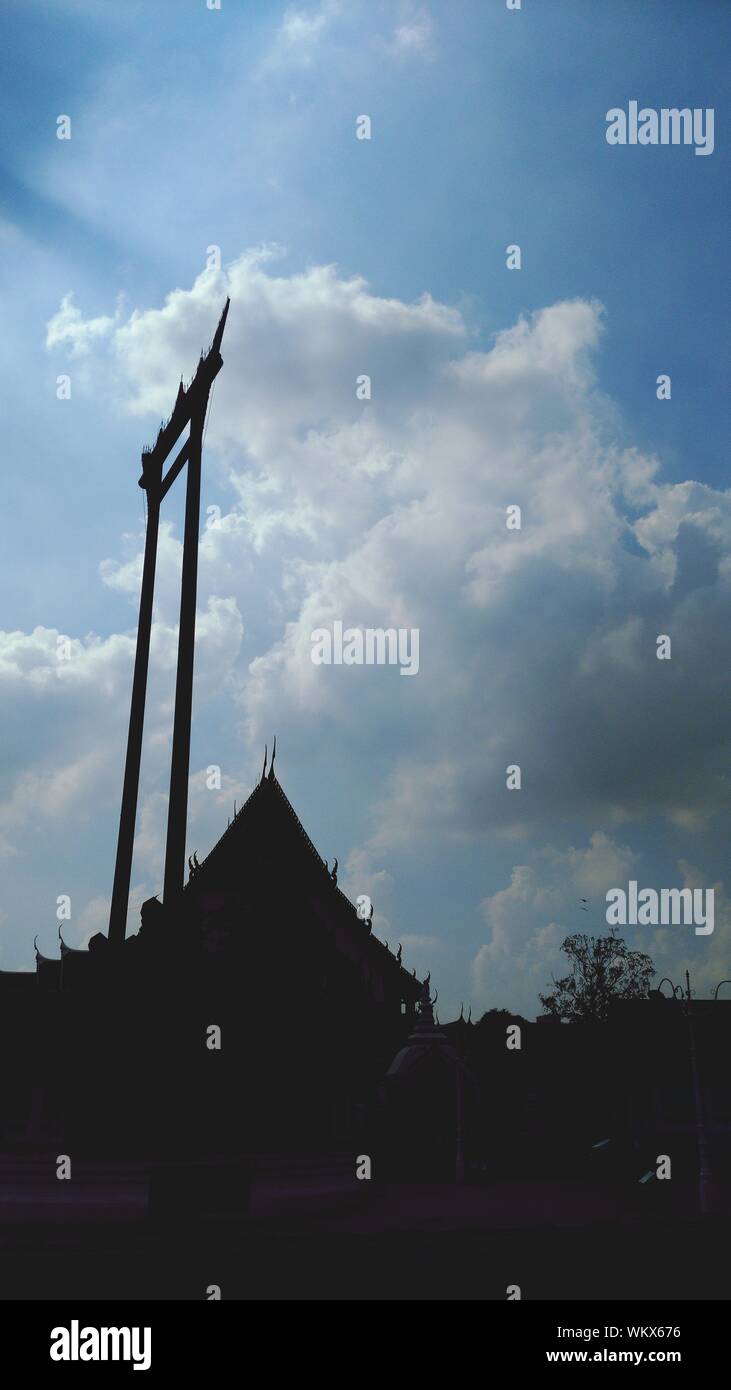 Basso angolo vista di Silhouette altalena gigante di Wat Suthat Tempio contro il cielo nuvoloso Foto Stock
