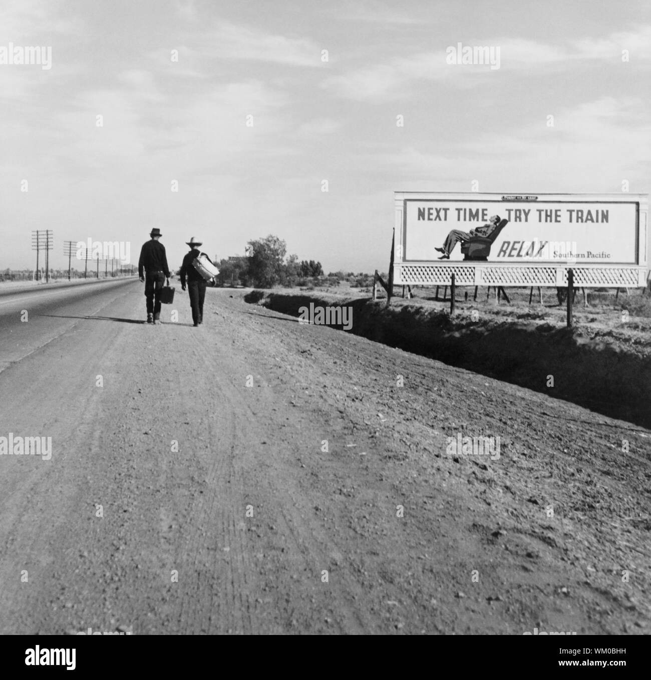 Vista posteriore di due uomini in cammino verso Los Angeles, California, USA, sulla strada sterrata nei pressi di affissioni che dice "la prossima volta provare il treno. Rilassatevi.', Dorothea Lange, U.S. Farm Security Administration, Marzo 1937 Foto Stock