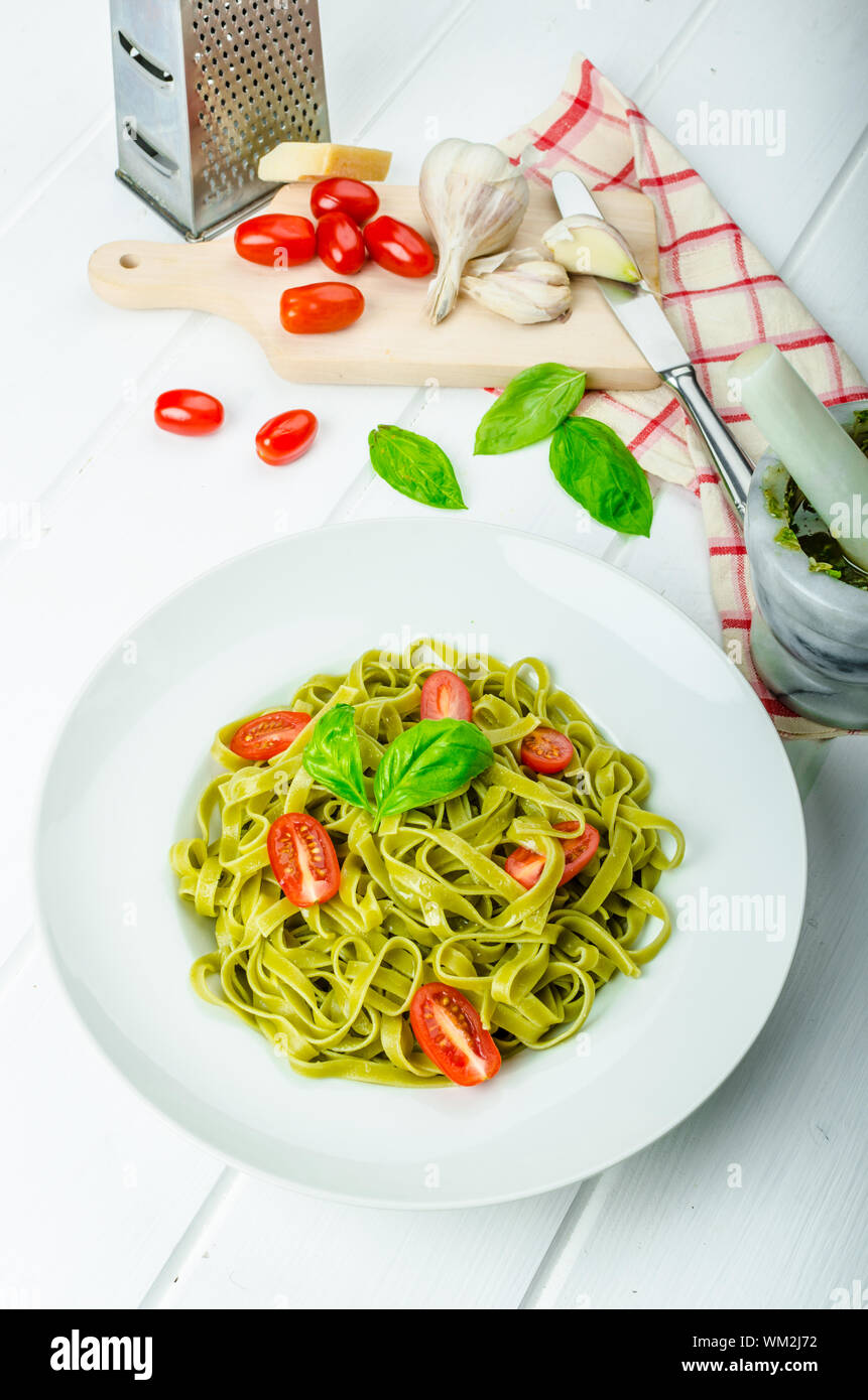 Gli spinaci tagliatelle al pesto di basilico e mini pomodori, wood board, tovaglioli e pesto mortaio Foto Stock