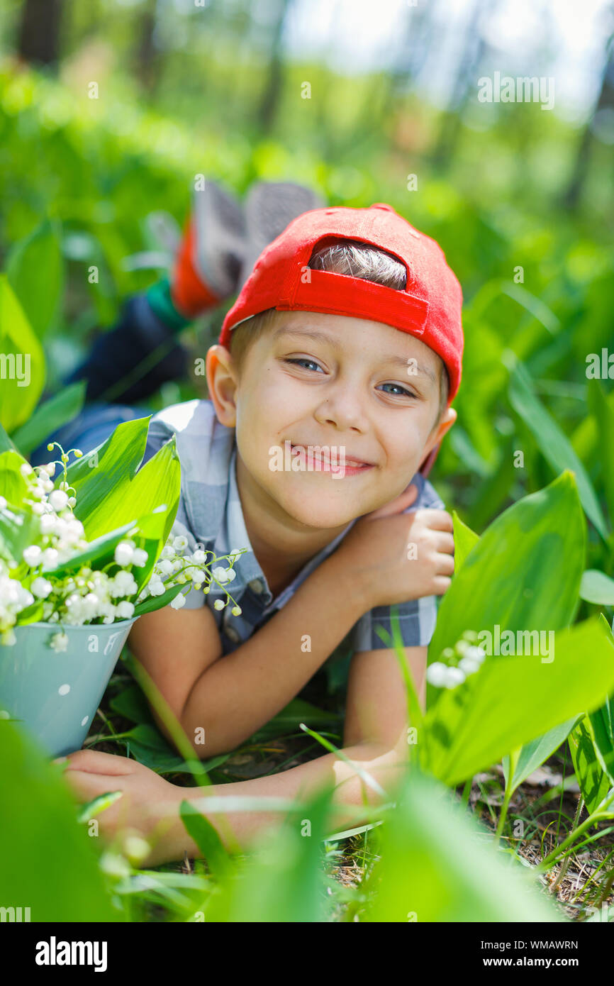 Carino piccolo ragazzo con gigli della valle nella foresta sul giorno di primavera Foto Stock
