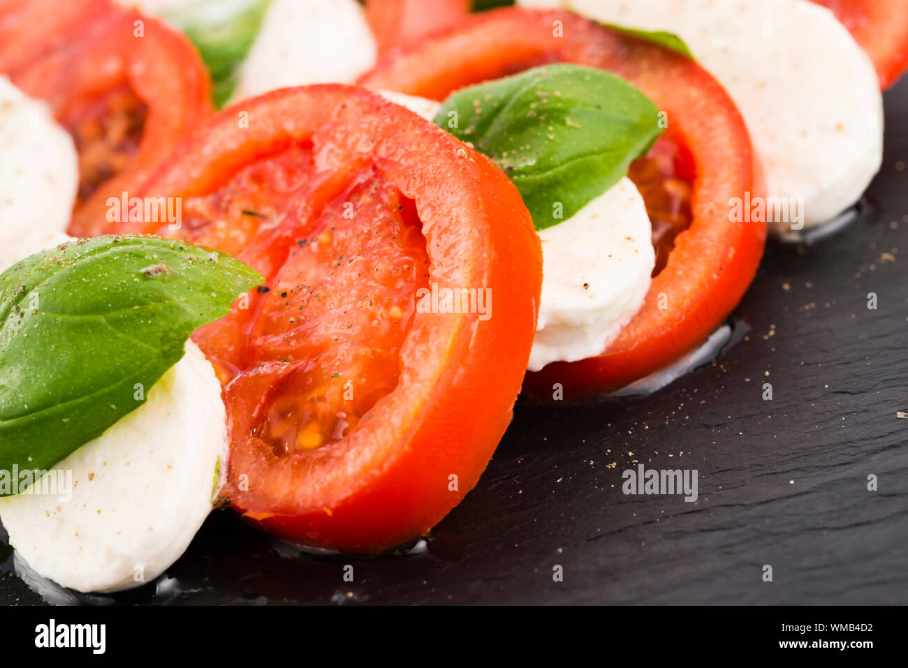 Insalata caprese con mozzarella, pomodoro, basilico e aceto balsamico e disposti sulla piastra nera Foto Stock