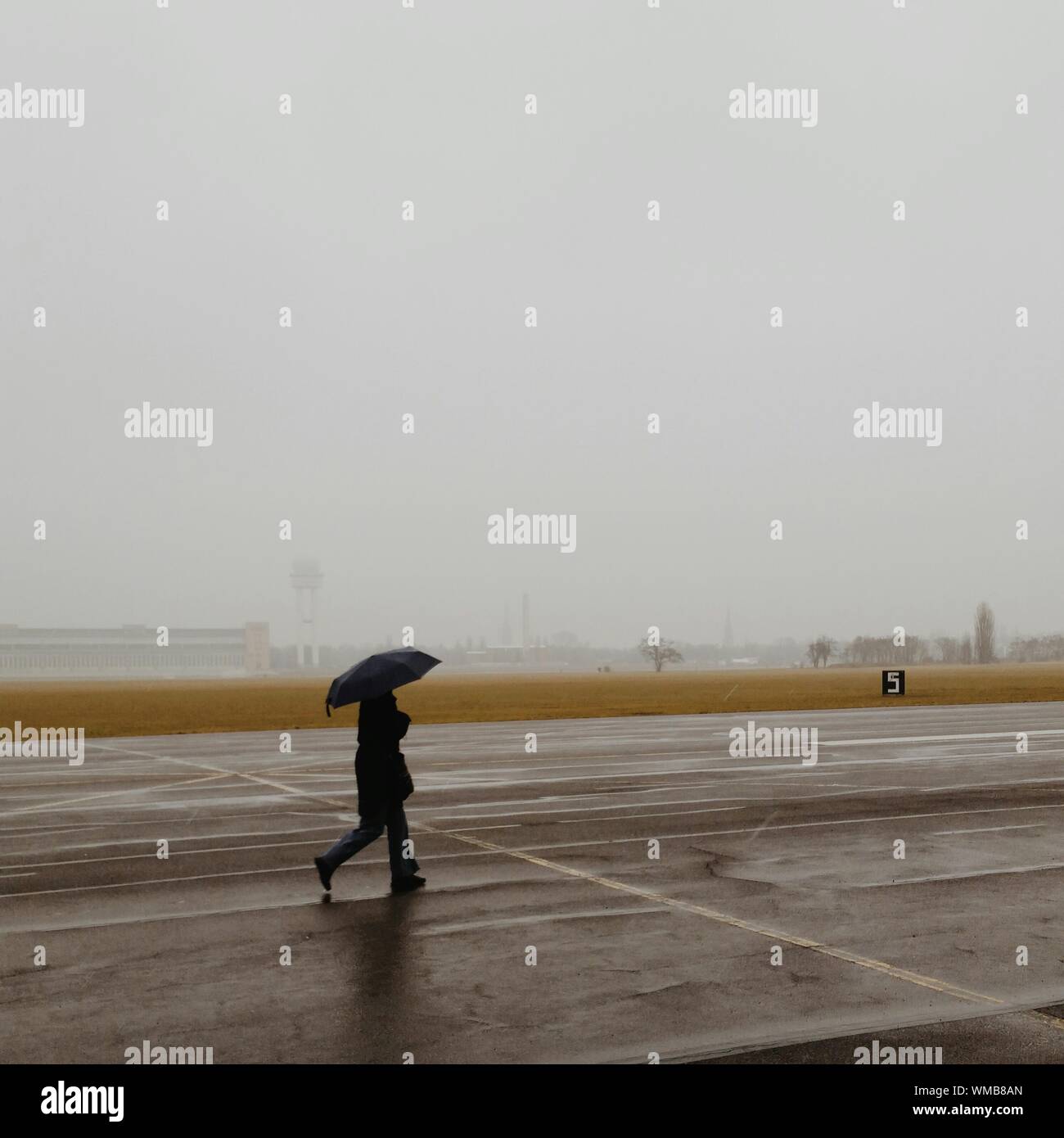 Uomo con ombrello camminando sulla pista di aeroporto contro il cielo  chiaro Foto stock - Alamy