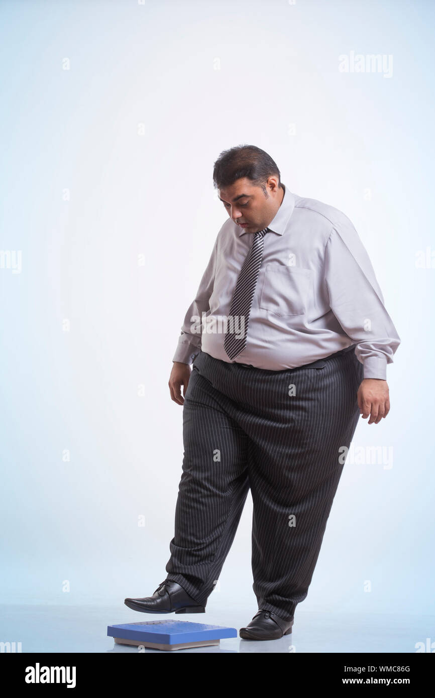 Obeso di indossare abiti formali stepping sulla macchina di pesatura Foto Stock