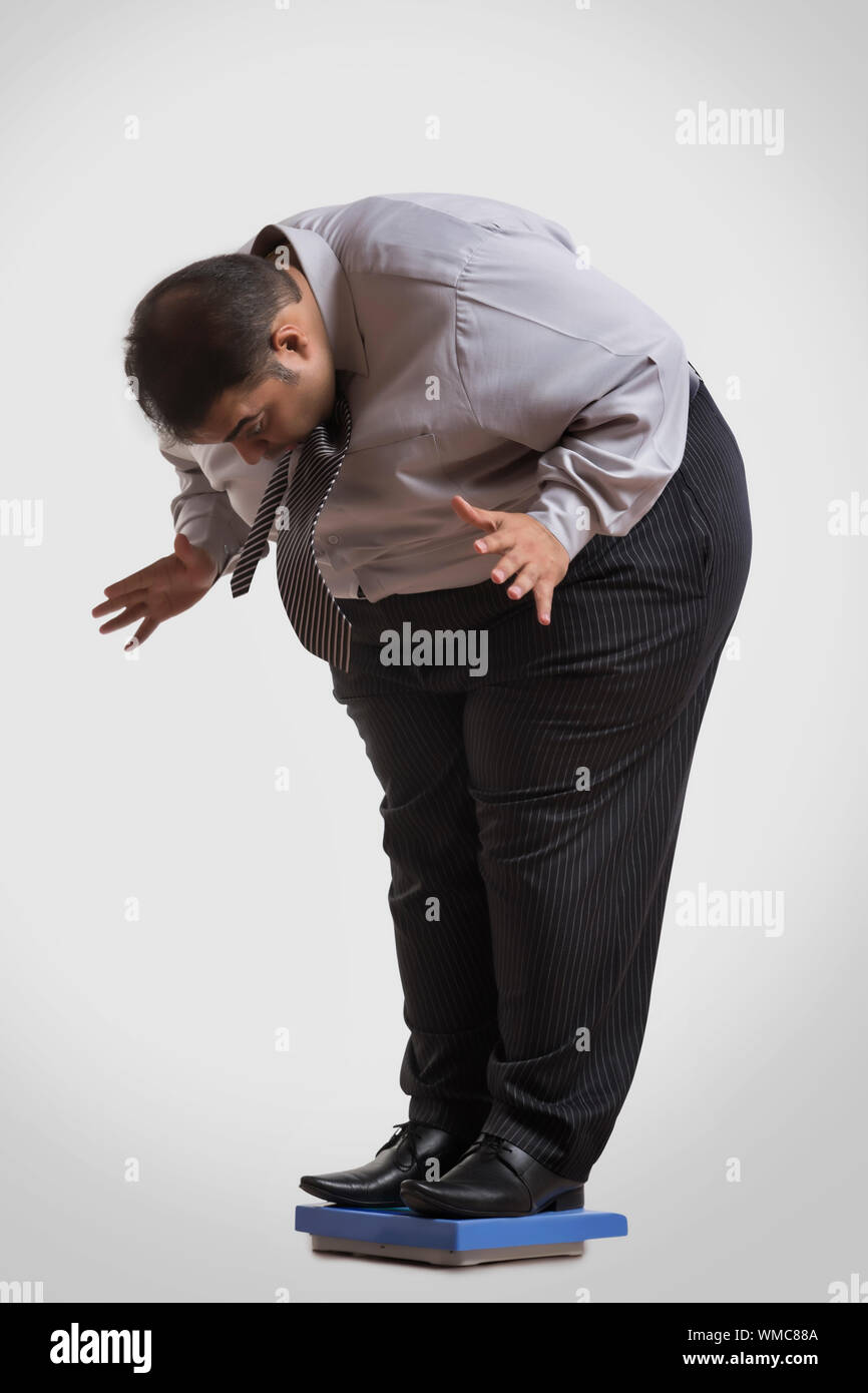 Uomo obesi in abiti formali in piedi su una macchina di pesatura in avanti di piegatura scioccato di vedere il suo peso Foto Stock
