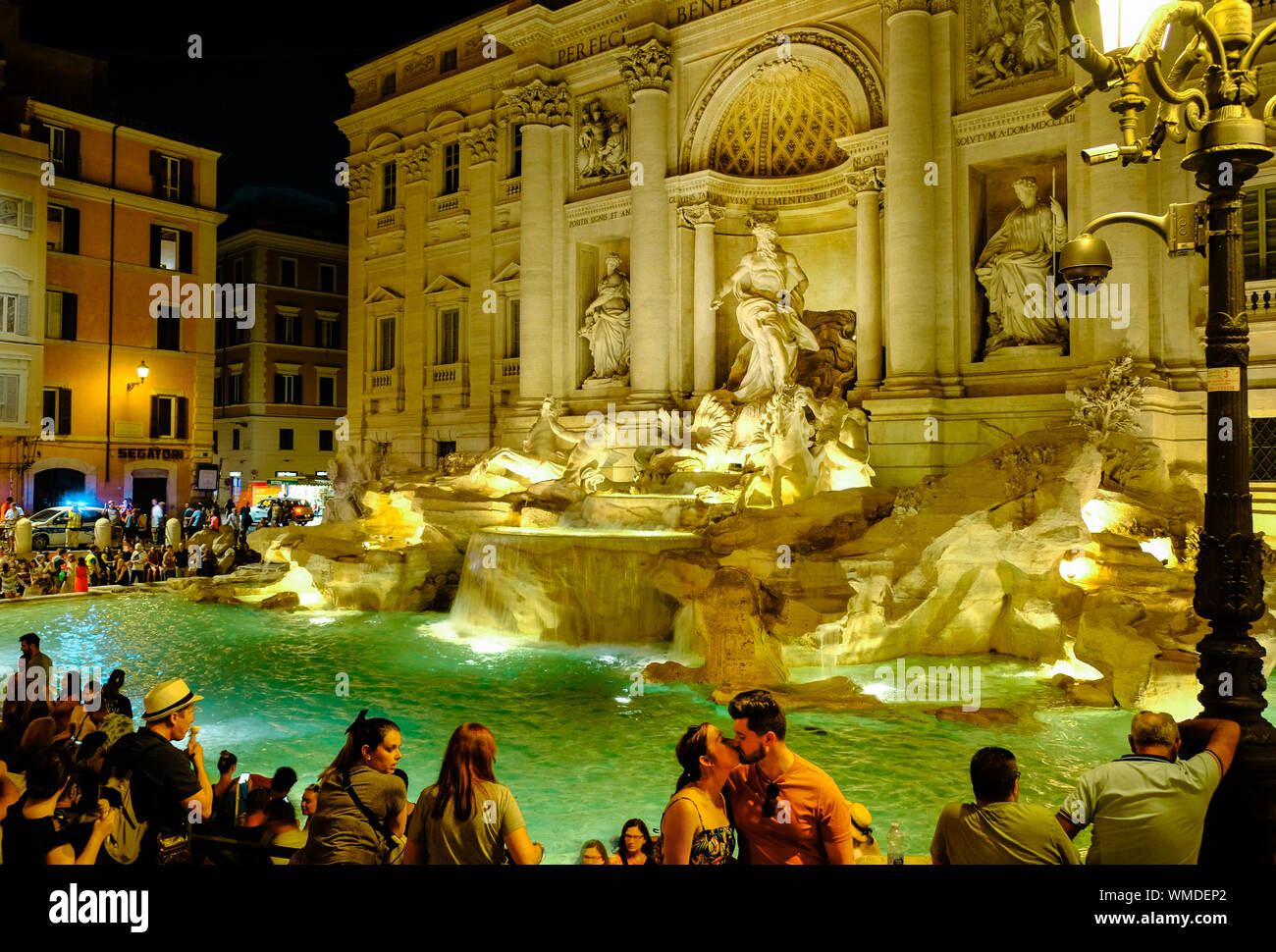 Vista notturna della bellissima Fontana di Trevi circondato con persone; coppia giovane sulla destra kissing Foto Stock