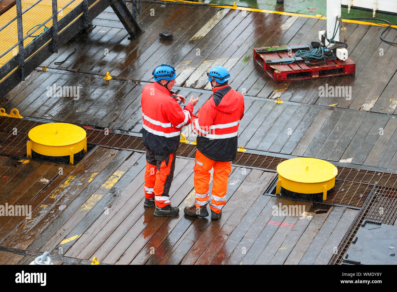 Per gli operai che indossa caschi di sicurezza e indumenti da lavoro riflettente avente una discussione sul ponte di SD Nord del Fiume nave da carico, King George V dock, Gl Foto Stock