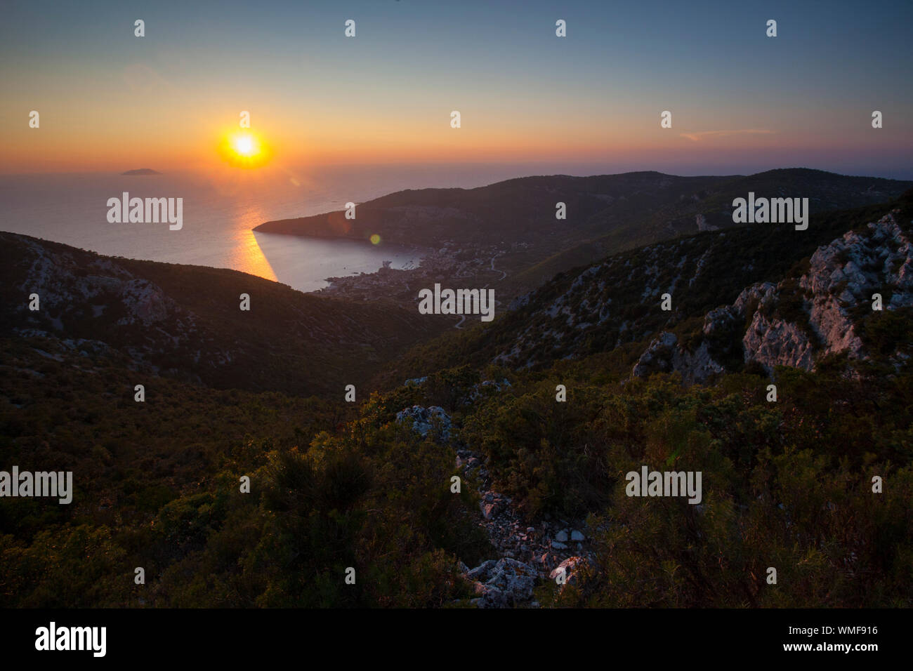 Tramonto dal Monte Hum con Komiza città in distanza, isola di Vis, Croazia. Foto Stock