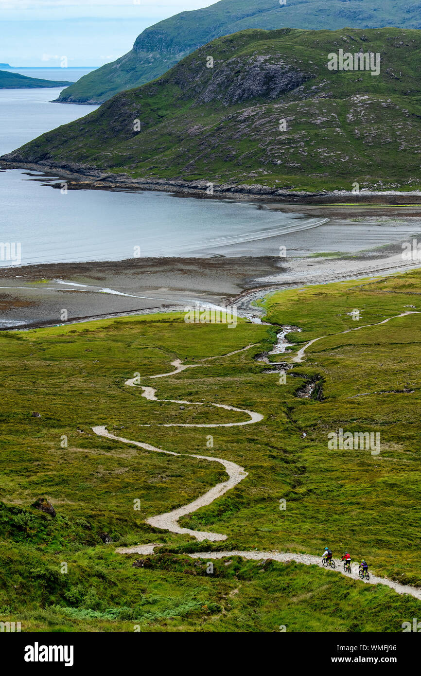 Tre i ciclisti di montagna corsa giù per un sentiero per Camasunary Beach sull'Isola di Skye sulla costa ovest della Scozia durante l'estate. Foto Stock