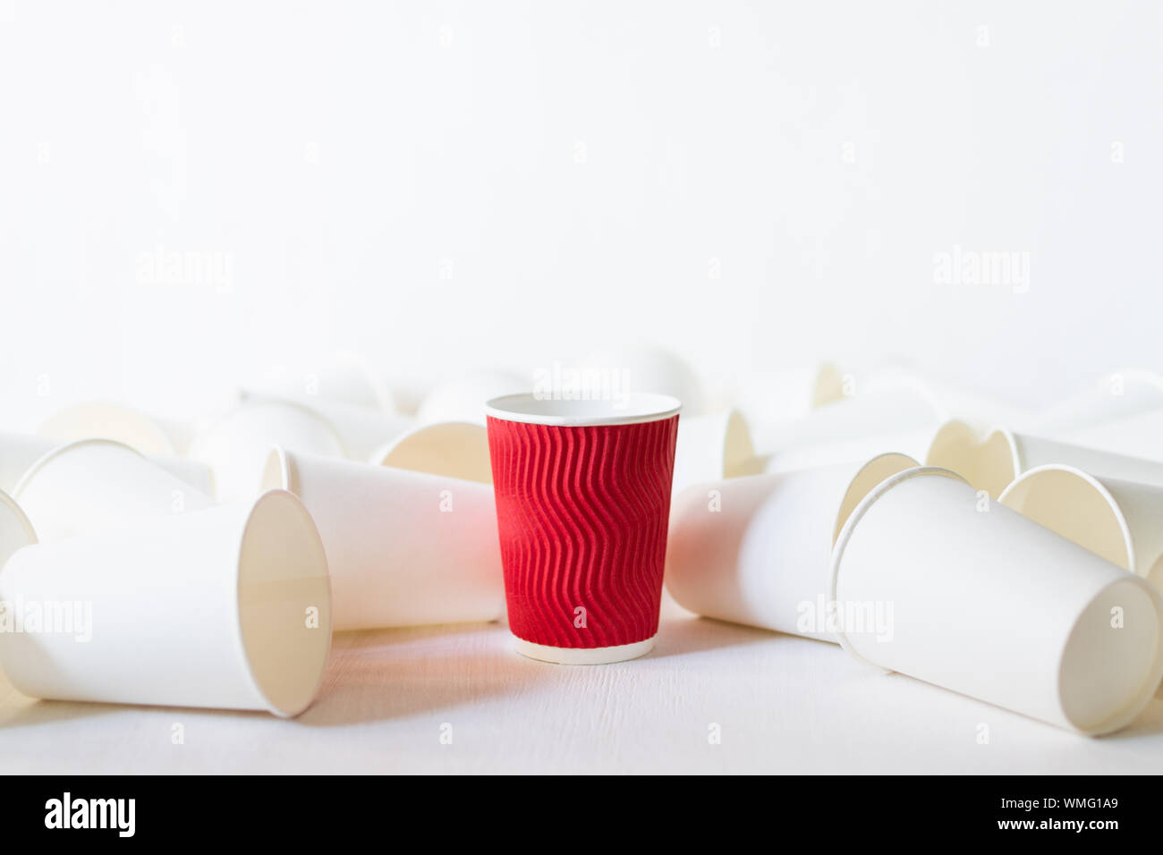 Carta rossa tazza di caffè si erge tra giacente white paper cups. Sfondo bianco, spazio di copia Foto Stock