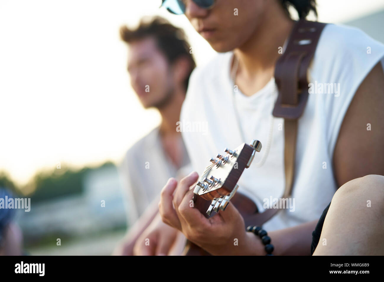 Giovani asiatici uomini adulti seduti sulla spiaggia rilassante e a suonare la chitarra Foto Stock