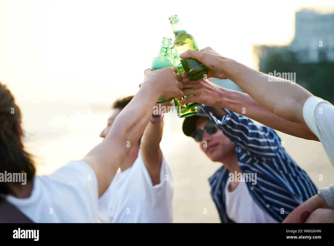 Un gruppo di giovani asiatici uomini adulti seduti sulla spiaggia la tostatura con bottiglie di birra Foto Stock