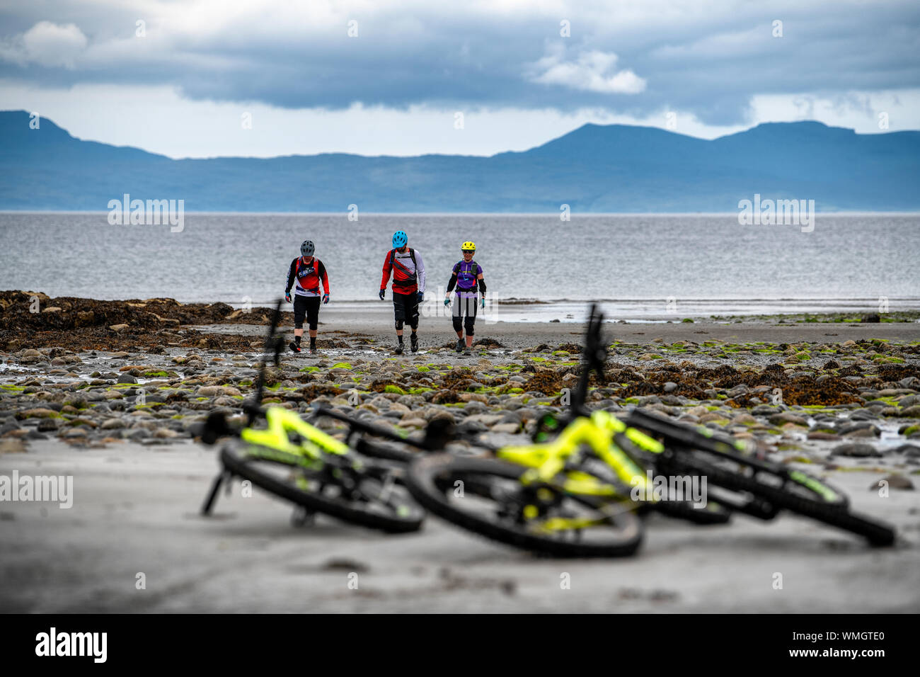 Due uomini e una donna lasciano le loro mountain bike per una passeggiata sulla spiaggia Camasunary sull'Isola di Skye durante l'estate. Foto Stock