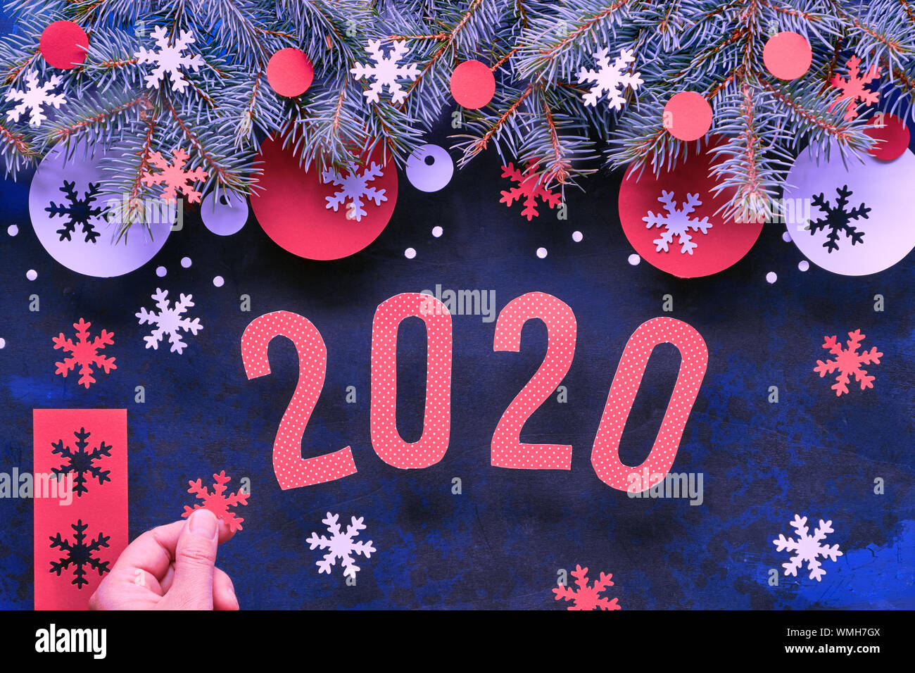 Mano che tiene la carta il simbolo del fiocco di neve. Natale o Capodanno lo sfondo con il numero 2020, ramoscelli di abete rosso e bianco decorazioni di carta. Appartamento laico, vista dall'alto su dar Foto Stock