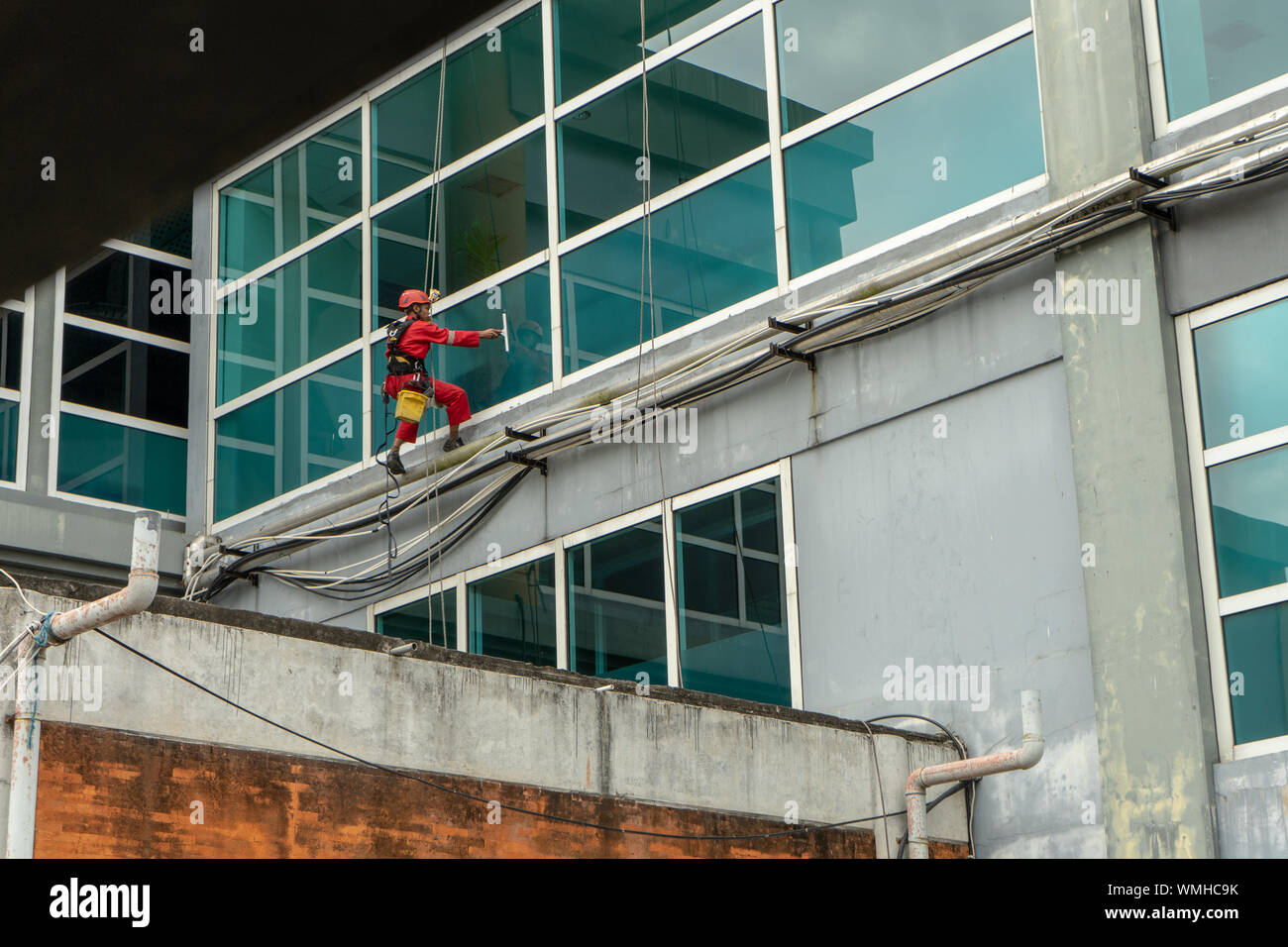 DENPASAR/Bali, Indonesia-Agosto 26 2019: portieri o servizio di pulizia sono stati pulizia del vetro si trova all'altezza di un edificio utilizzando safet completo Foto Stock