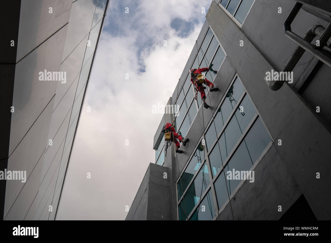 DENPASAR/Bali, Indonesia-Agosto 26 2019: portieri o servizio di pulizia sono stati pulizia del vetro si trova all'altezza di un edificio utilizzando safet completo Foto Stock