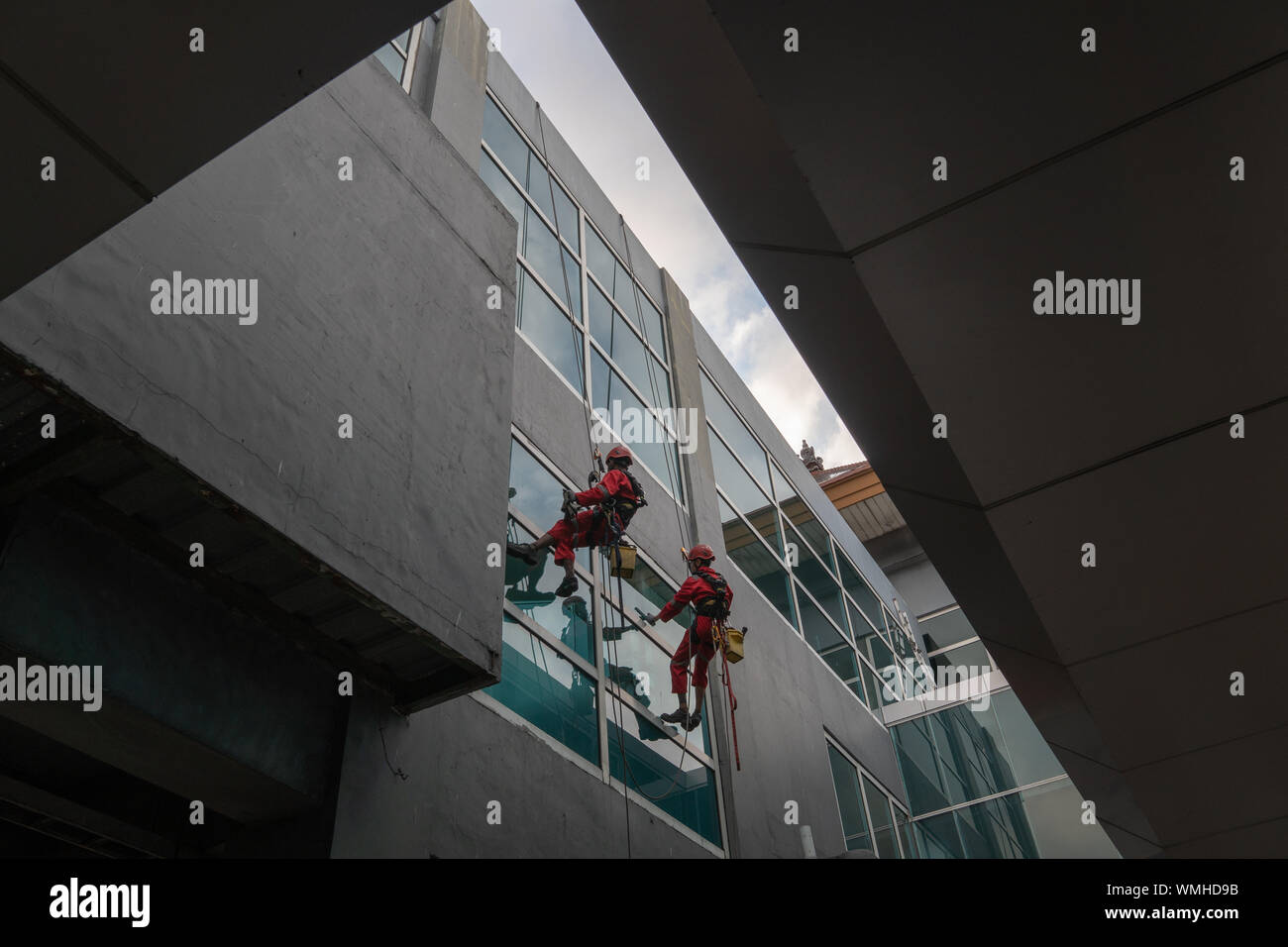 DENPASAR/Bali, Indonesia-Agosto 26 2019: portieri o servizio di pulizia sono stati pulizia del vetro si trova all'altezza di un edificio utilizzando safet completo Foto Stock