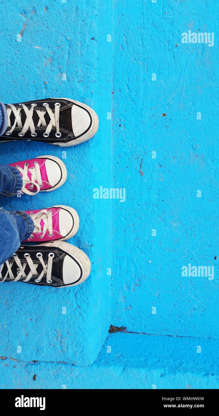 Vista dei bambini piedi indossando tela rosa tra l'altro piede sul fasi blu Foto Stock