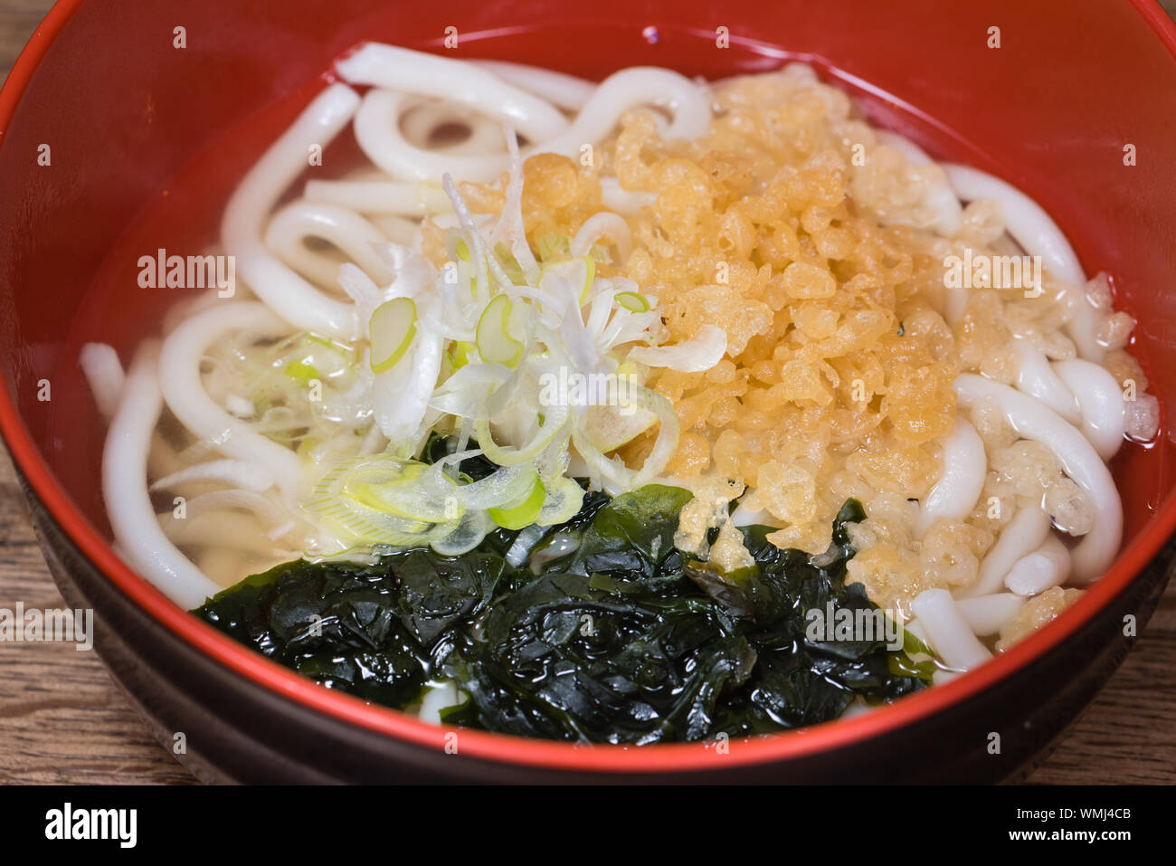 Udon in brodo con alghe wakame, Tenkasu, cipolline, brodo di pesce in una ciotola rossa Foto Stock