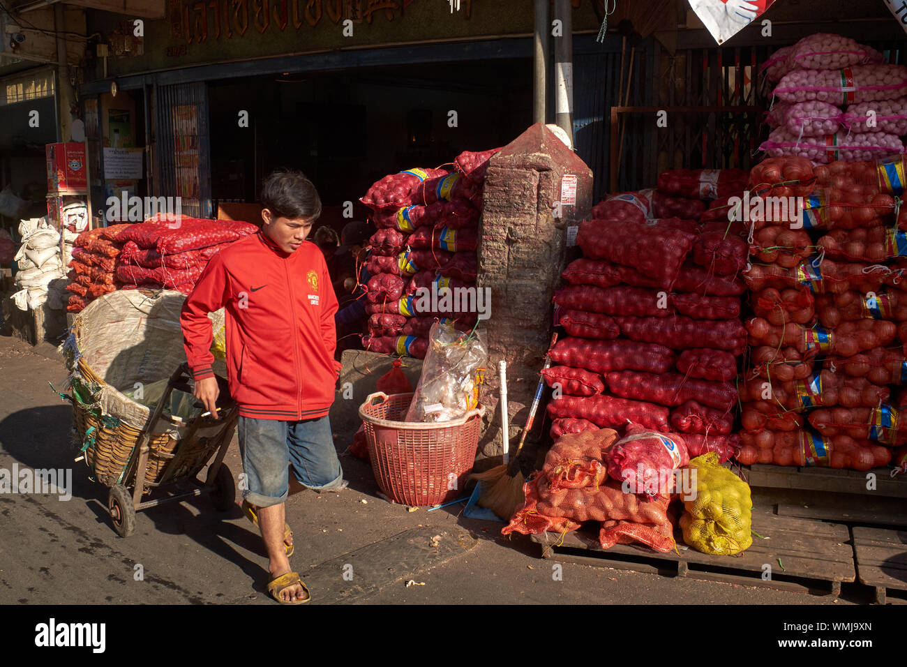 Un Myanmarese (Burmese) helper di mercato a Pak Klong Talaat, un fiore & mercato ortofrutticolo a Bangkok, Thailandia, con sackfuls di cipolle in background Foto Stock