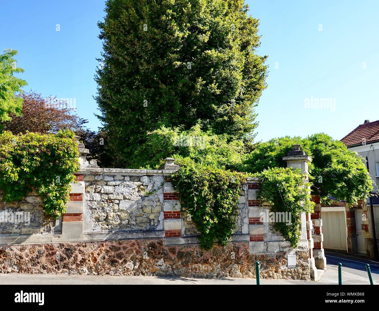 Vegetazione lussureggiante e alberi dietro una parete di mattoni, giardino nella piccola cittadina di Andrésy, Francia Foto Stock