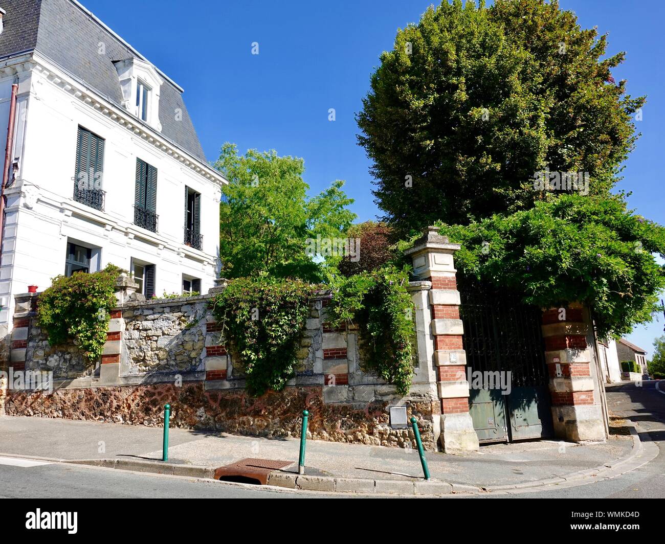 Vegetazione lussureggiante e alberi dietro una parete di mattoni, giardino nella piccola cittadina di Andrésy, Francia Foto Stock