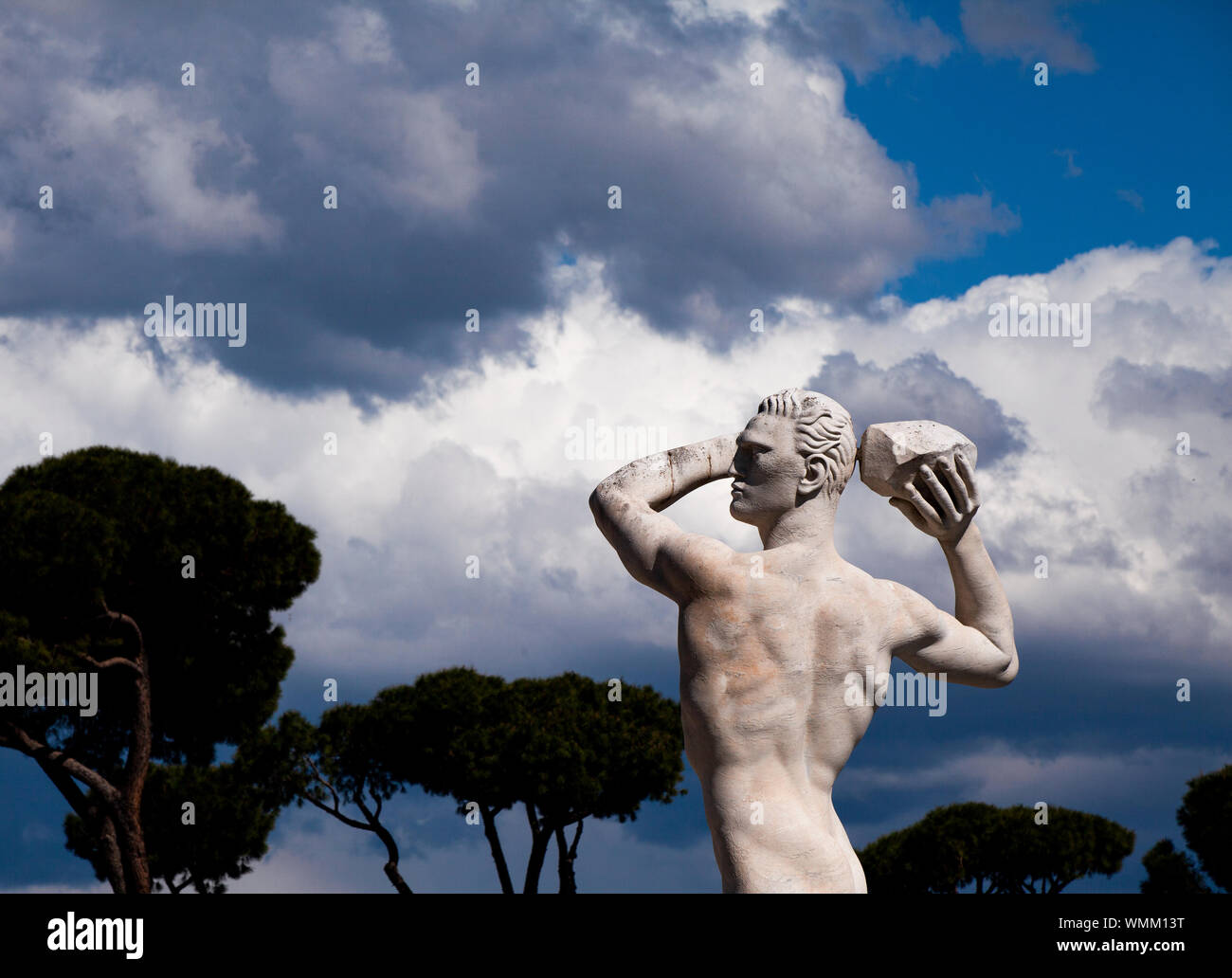 Una statua in pietra di uno sparo-putter nello Stadio dei Marmi a Roma. La statua ha le sue braccia sollevate, guardando in lontananza contro un cielo tempestoso estate Foto Stock