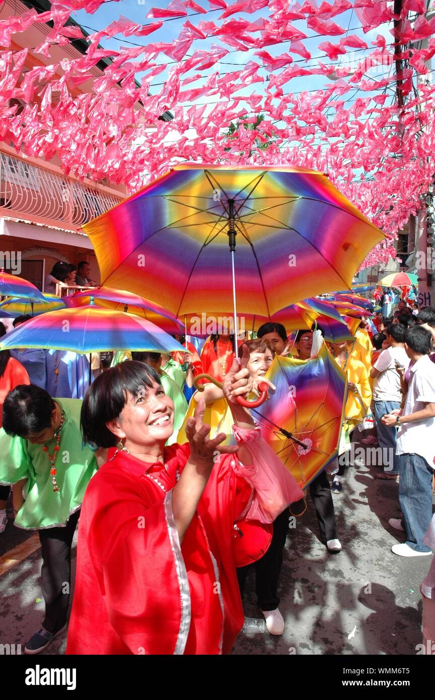 MANILA, Filippine - Lug 06, 2005: signora in abito rosso con ombrello coloratissimo in fiesta Foto Stock