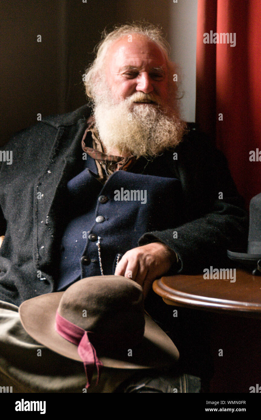 Un gentiluomo Vittoriano con un lungo occupato barba grigia, rilassante in una sala di un hotel in via principale al Sovereign Hill open-air-museum nel sobborgo Foto Stock
