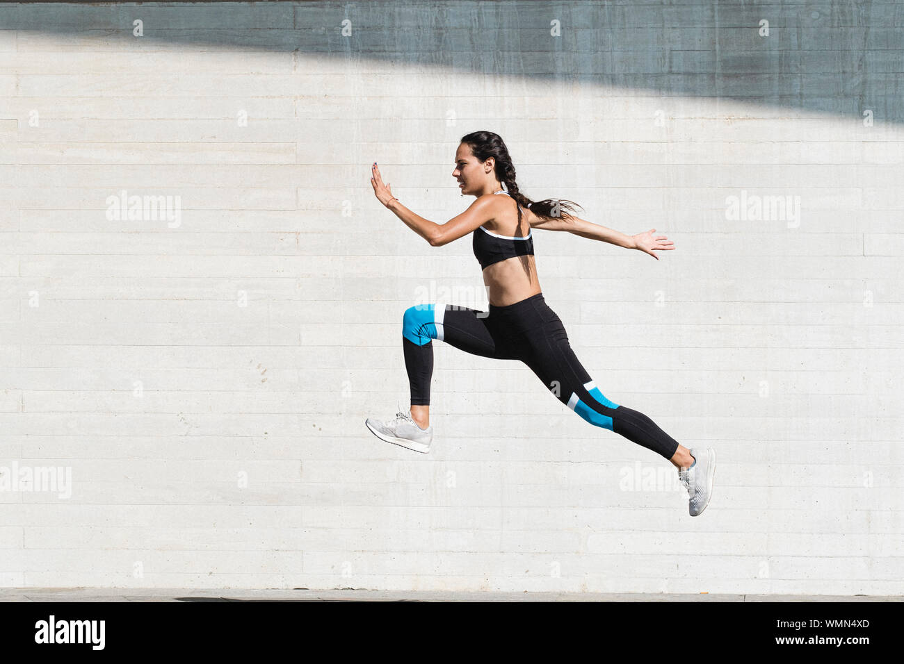 Corpo pieno di atleta femminile in sportswear saltando su calcestruzzo Foto Stock