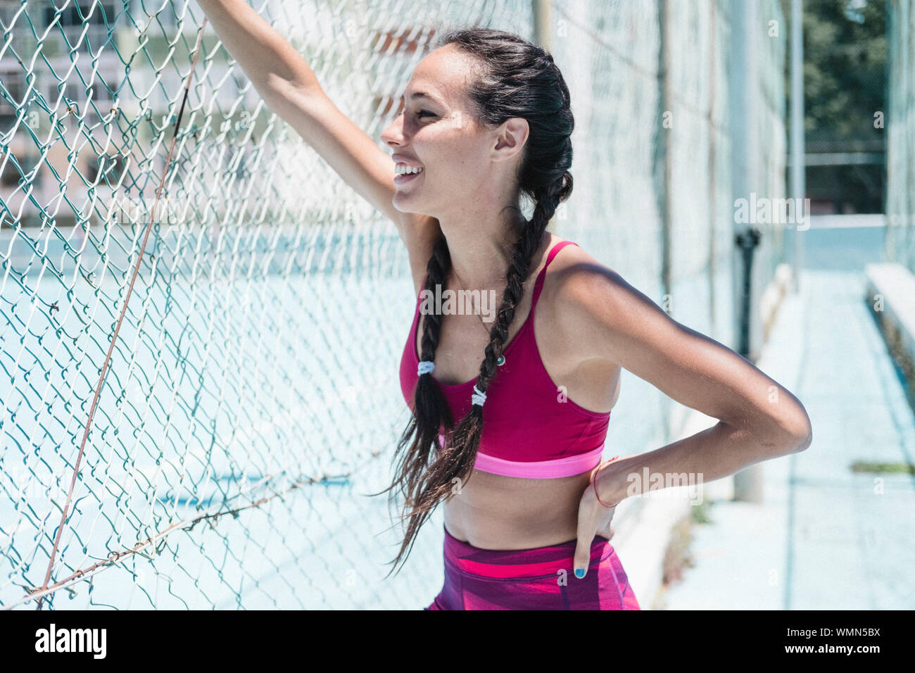 La parte superiore del corpo di smiley atleta femminile appoggiata sul recinto durante il riposo Foto Stock