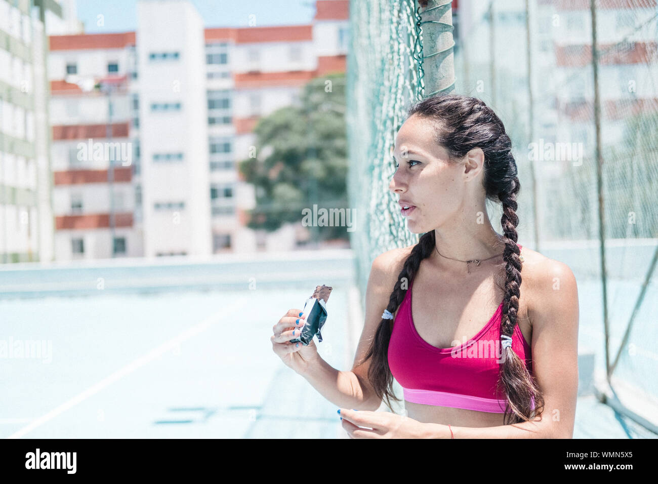 Immagine colorata di atleta femminile di mangiare un recovery bar su corte Foto Stock