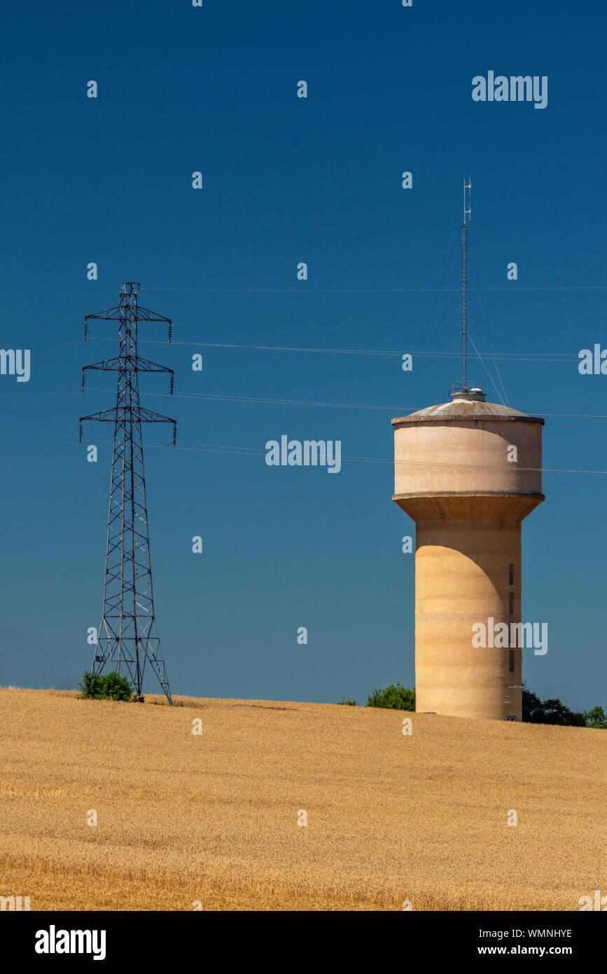Visualizzazione verticale di un calcestruzzo water tower a fianco di un traliccio di elettricità, sia in francese un campo di grano. Foto Stock