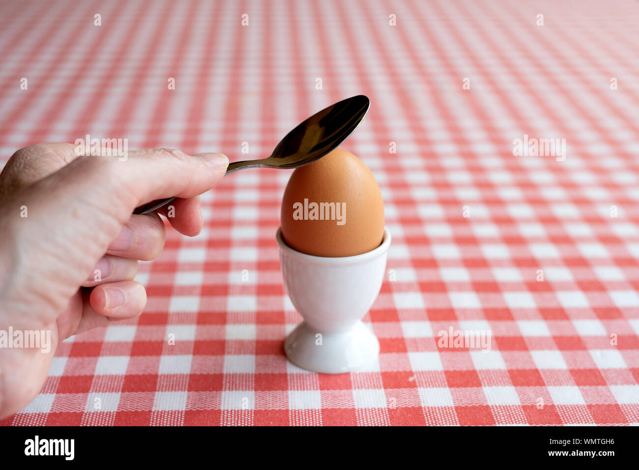 Mano che tiene un cucchiaio per rompere un uovo sodo Foto Stock