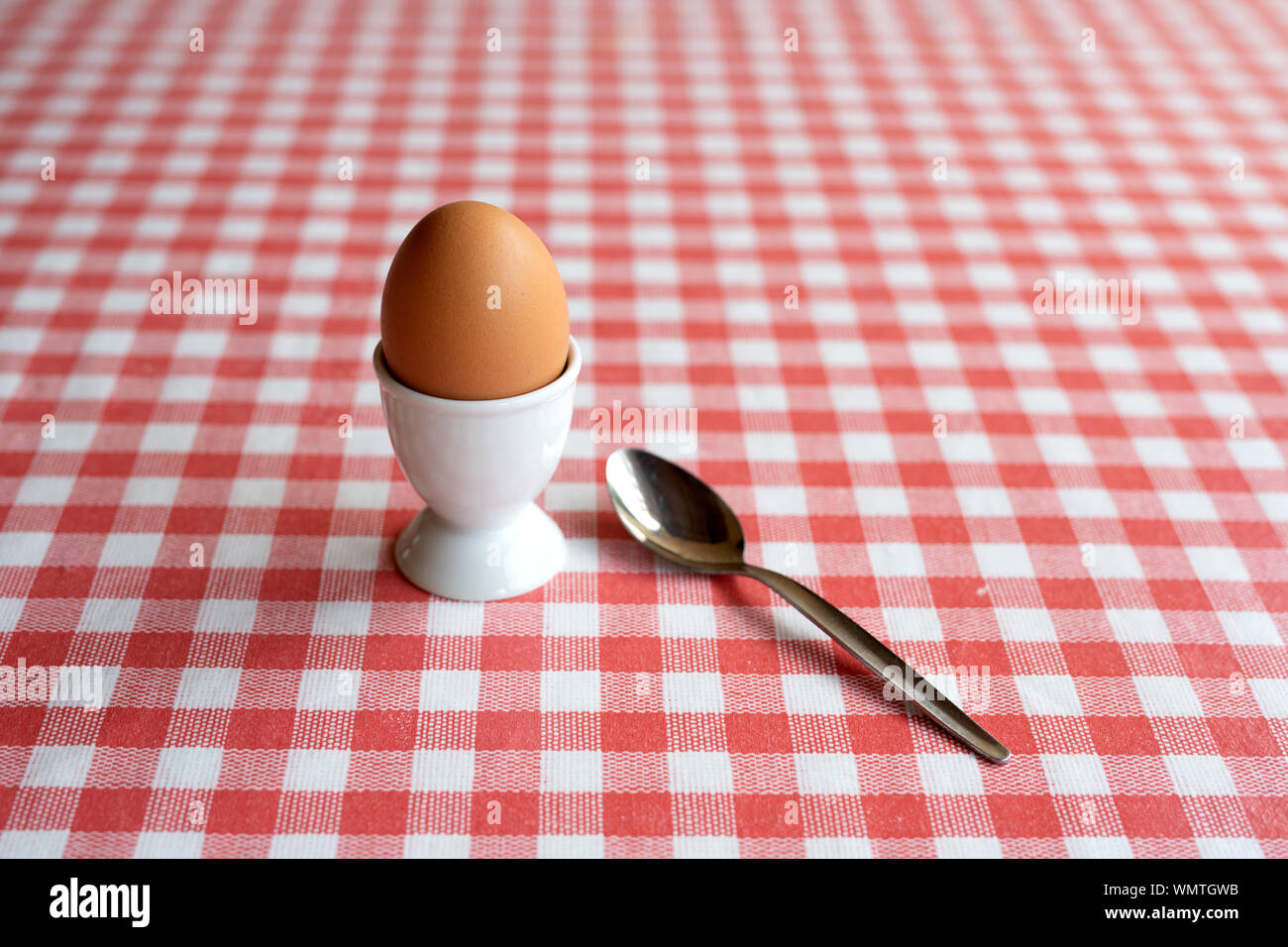Singolo uovo bollito con cucchiaio pronto a mangiare su un tavolo Foto Stock
