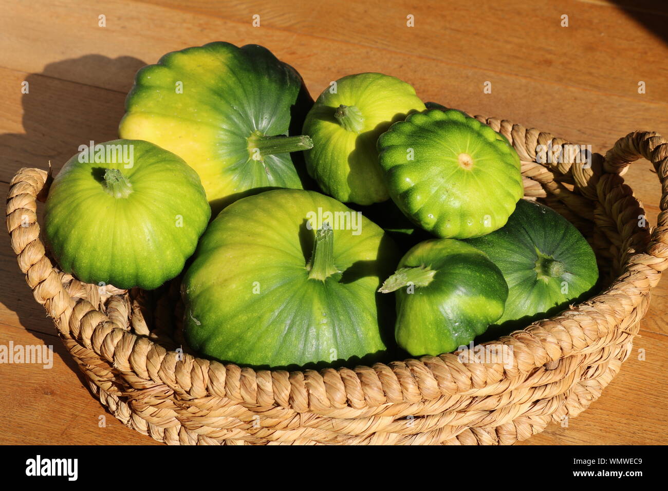 Green Patty pan smerlo refilato zucche di varie dimensioni in un basked al sole con pavimenti in rovere in background Foto Stock